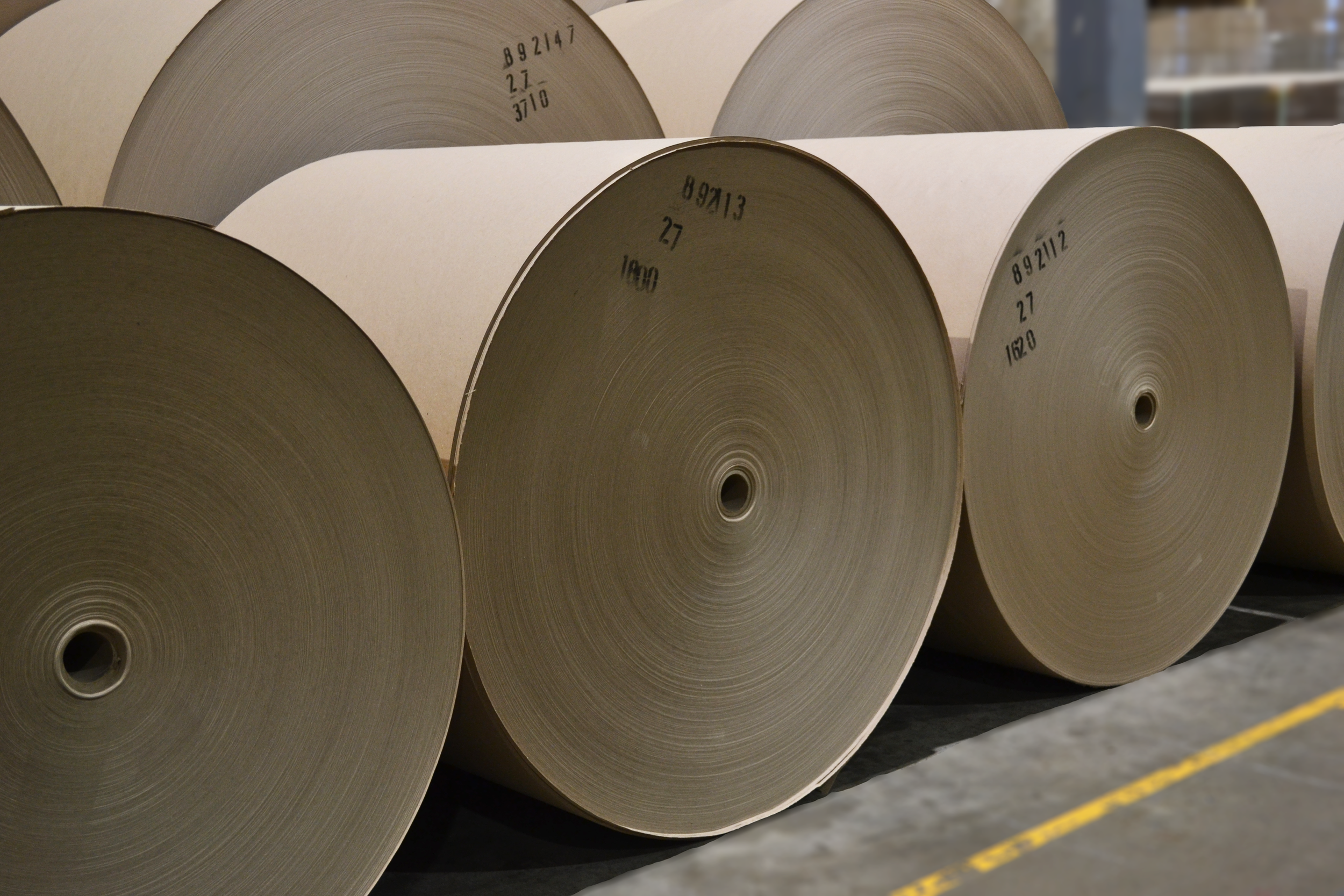 Large rolls of paper stacked in a warehouse, with markings and numbers on the sides.