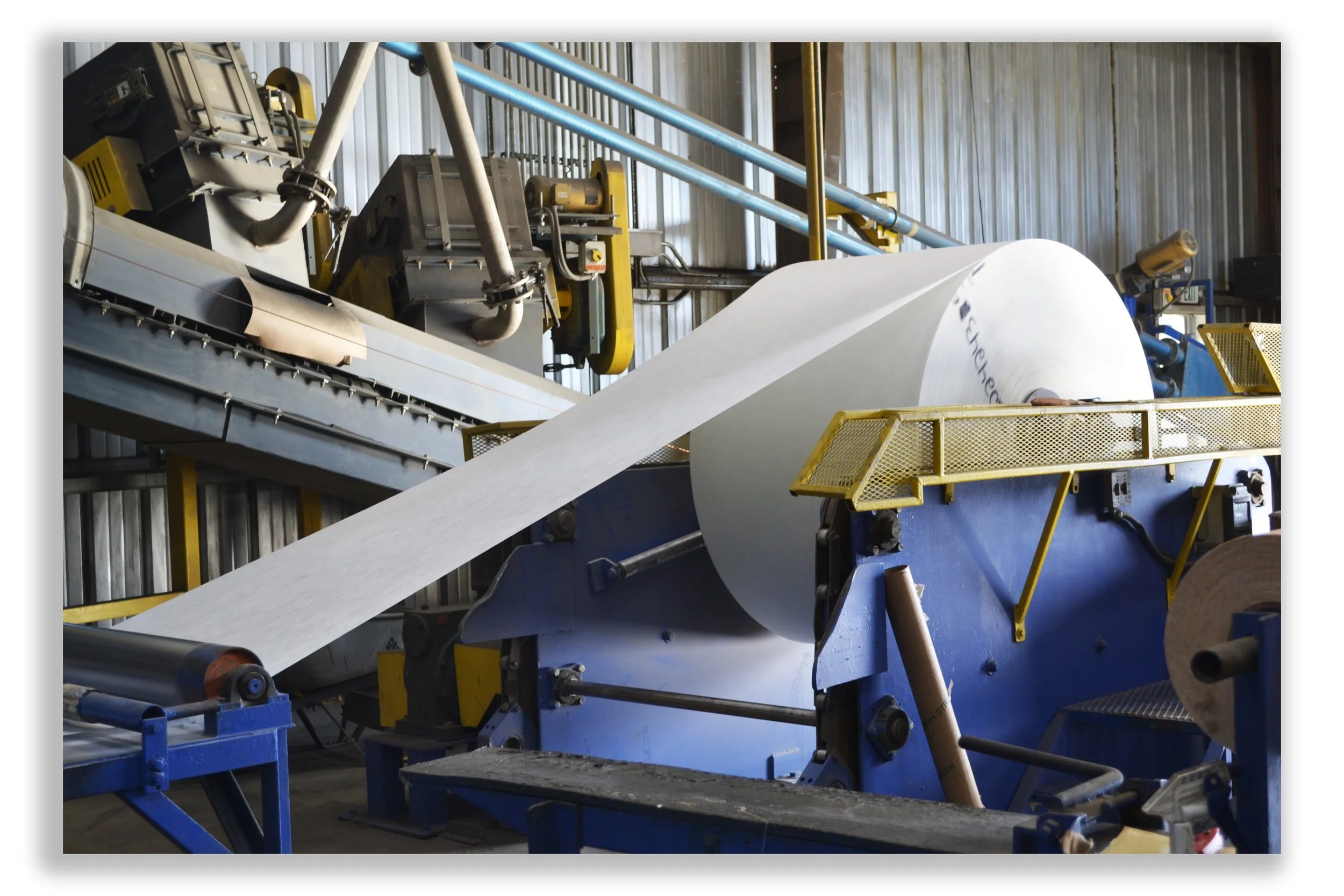 Industrial machine producing large rolls of paper in a factory setting.