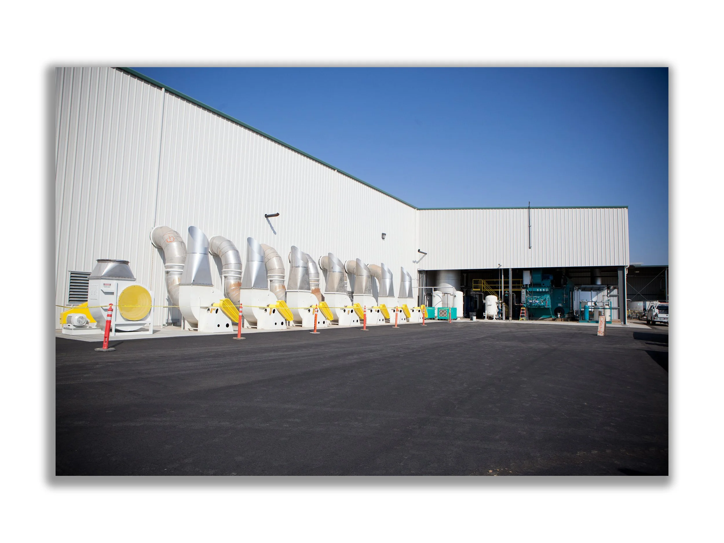 Industrial building with large ventilation ducts and equipment outside, clear blue sky in the background, paved asphalt ground.