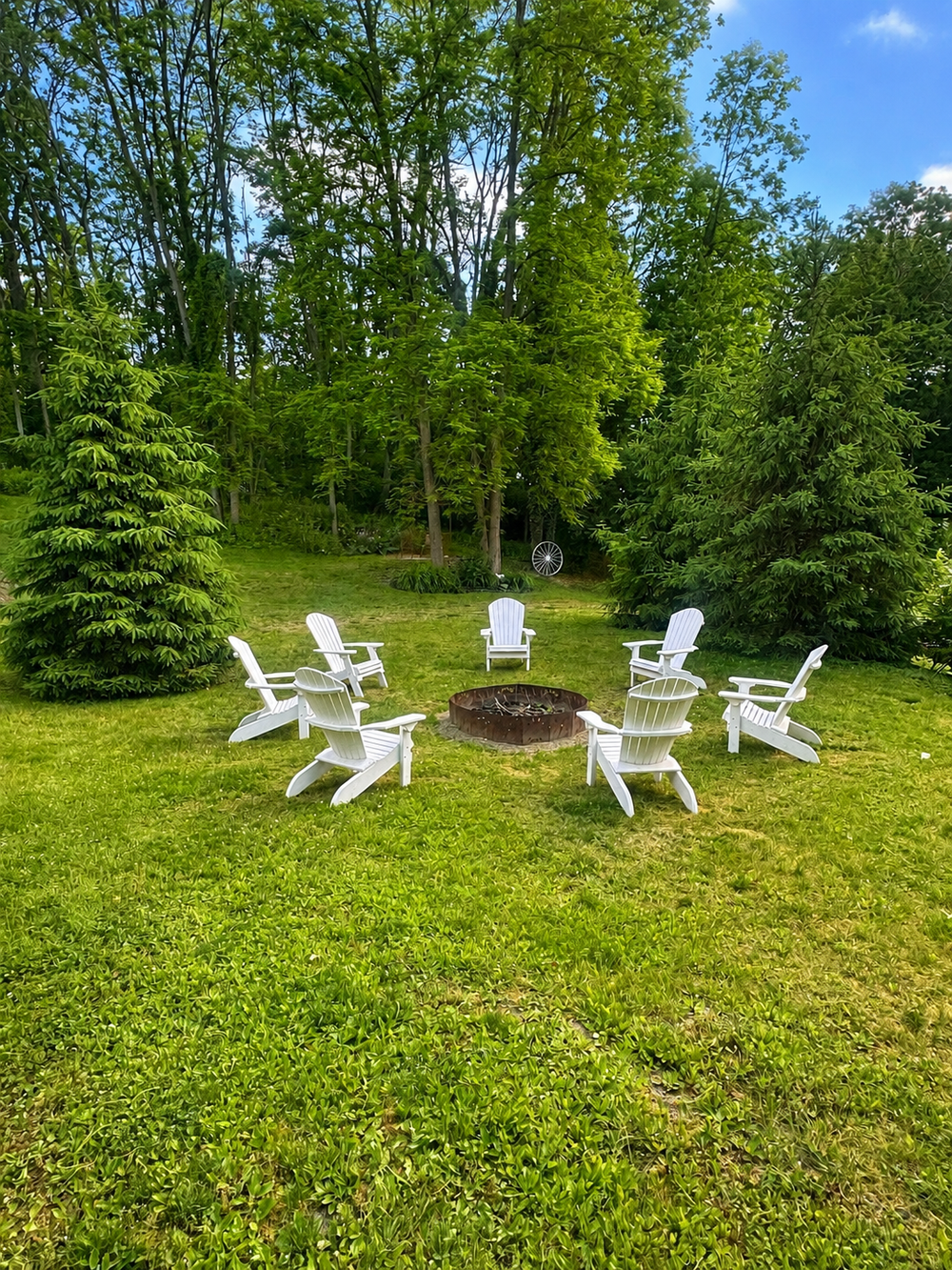 Backyard fire pit area with Adirondack chairs and open lawn space