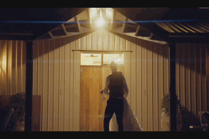 A couple standing in front of a wooden barn door, holding hands as the sun sets behind them.