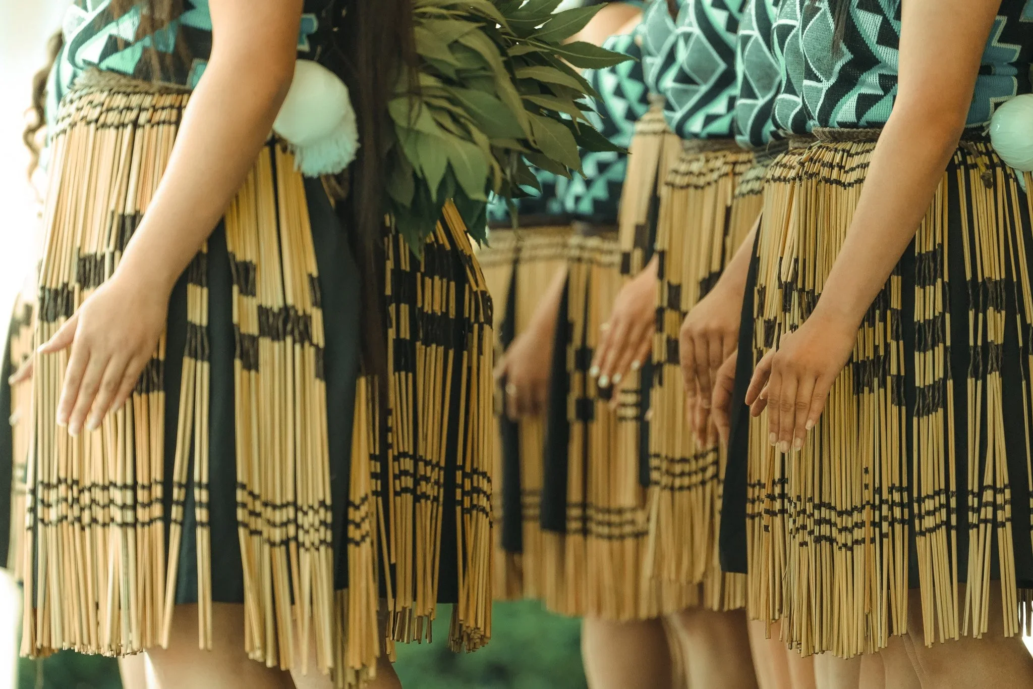 Group of women wearing traditional Polynesian attire with grass skirts, patterned tops, and floral adornments.