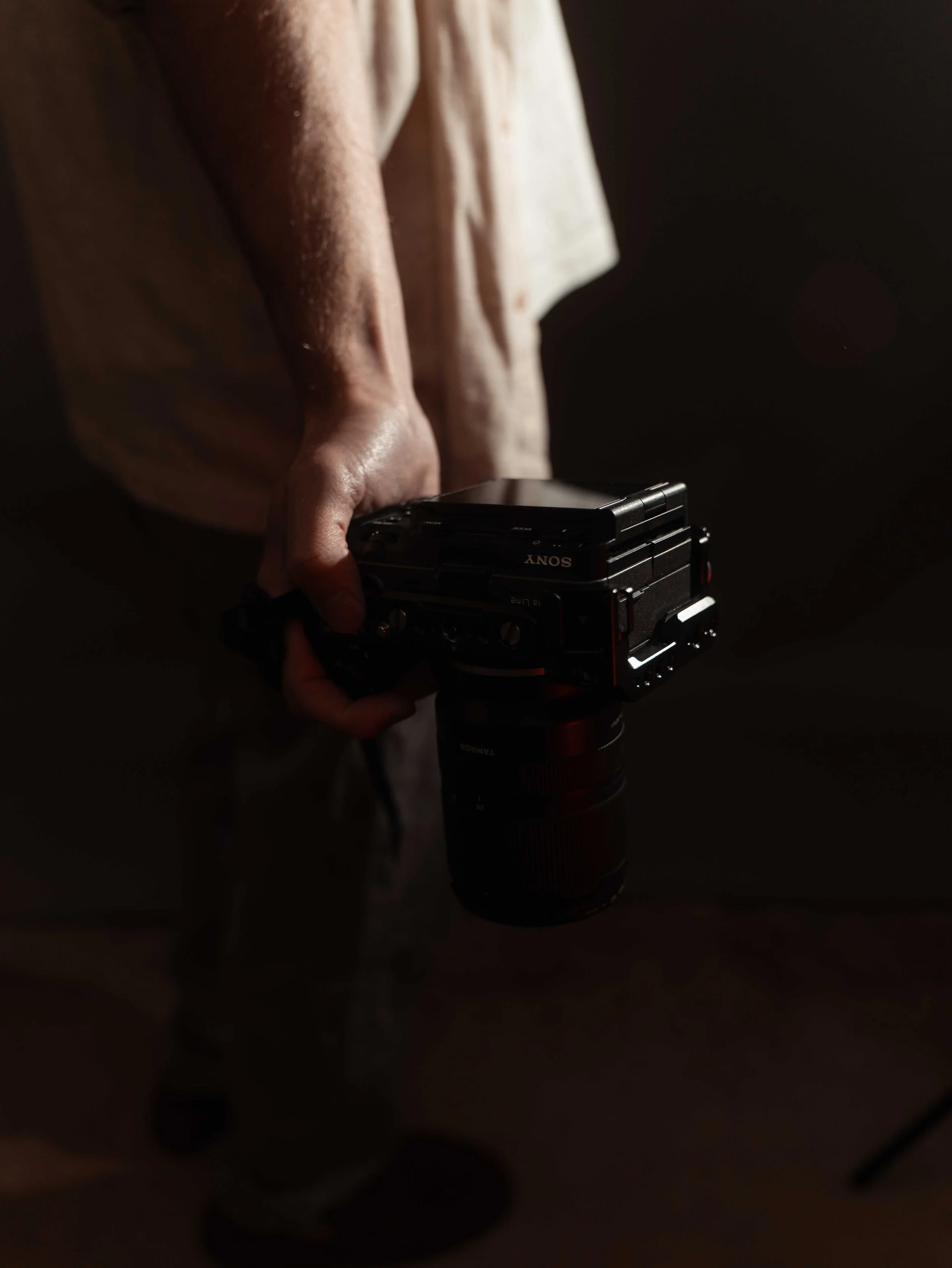 A person holding a Sony camera, with a dark background, illuminated by soft light.