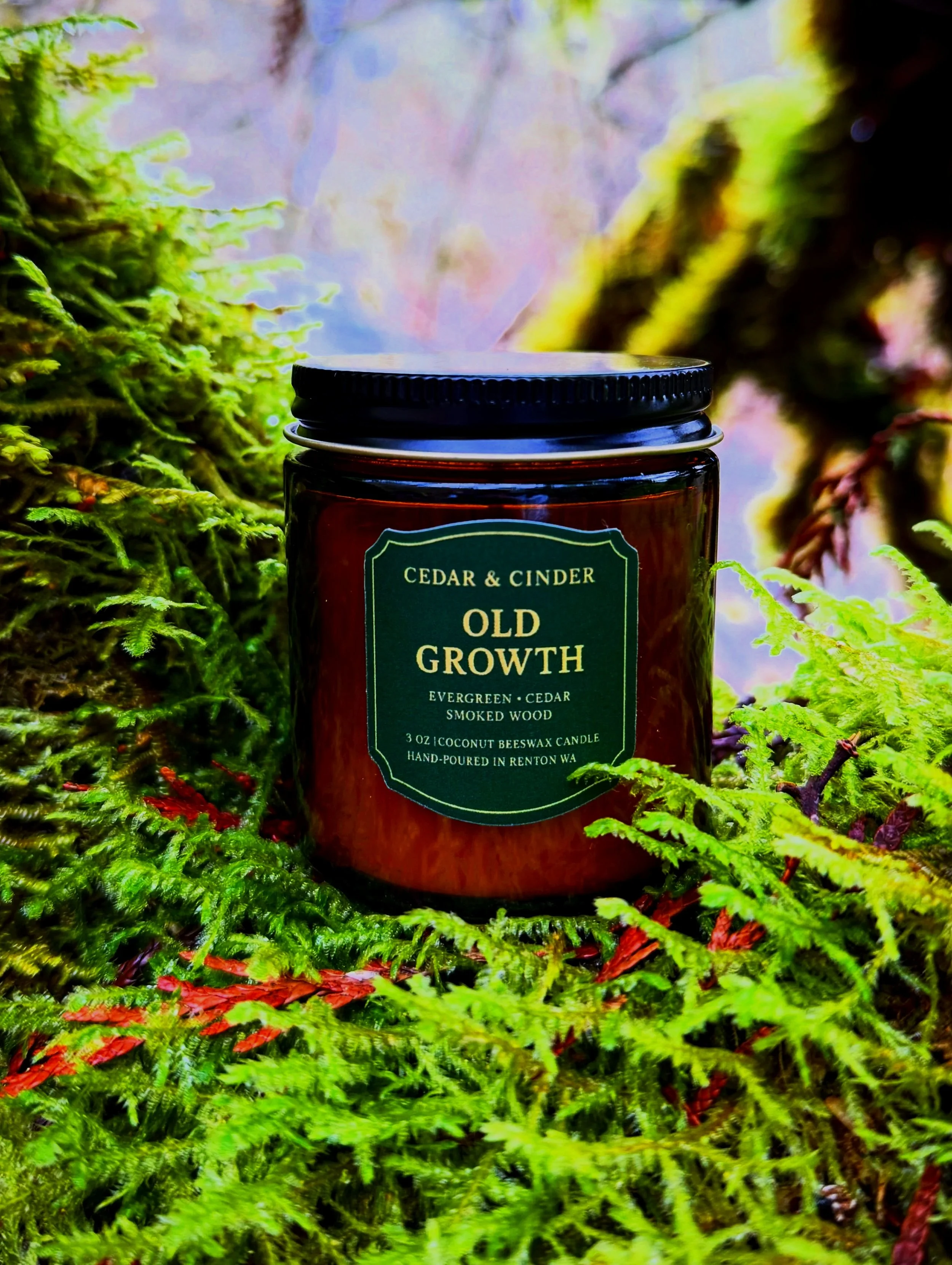 Close-up of a scented candle labeled Old Growth with a green background, cedar and smoked wood scent, in a brown jar with a metallic lid, placed on a shelf in Renton Washington.