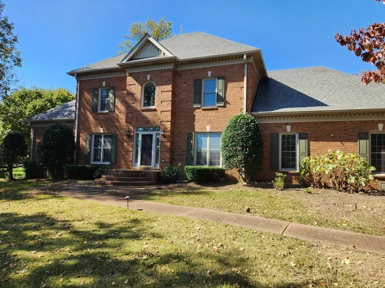 Front view of a two-story brick house with green shutters and a front yard.