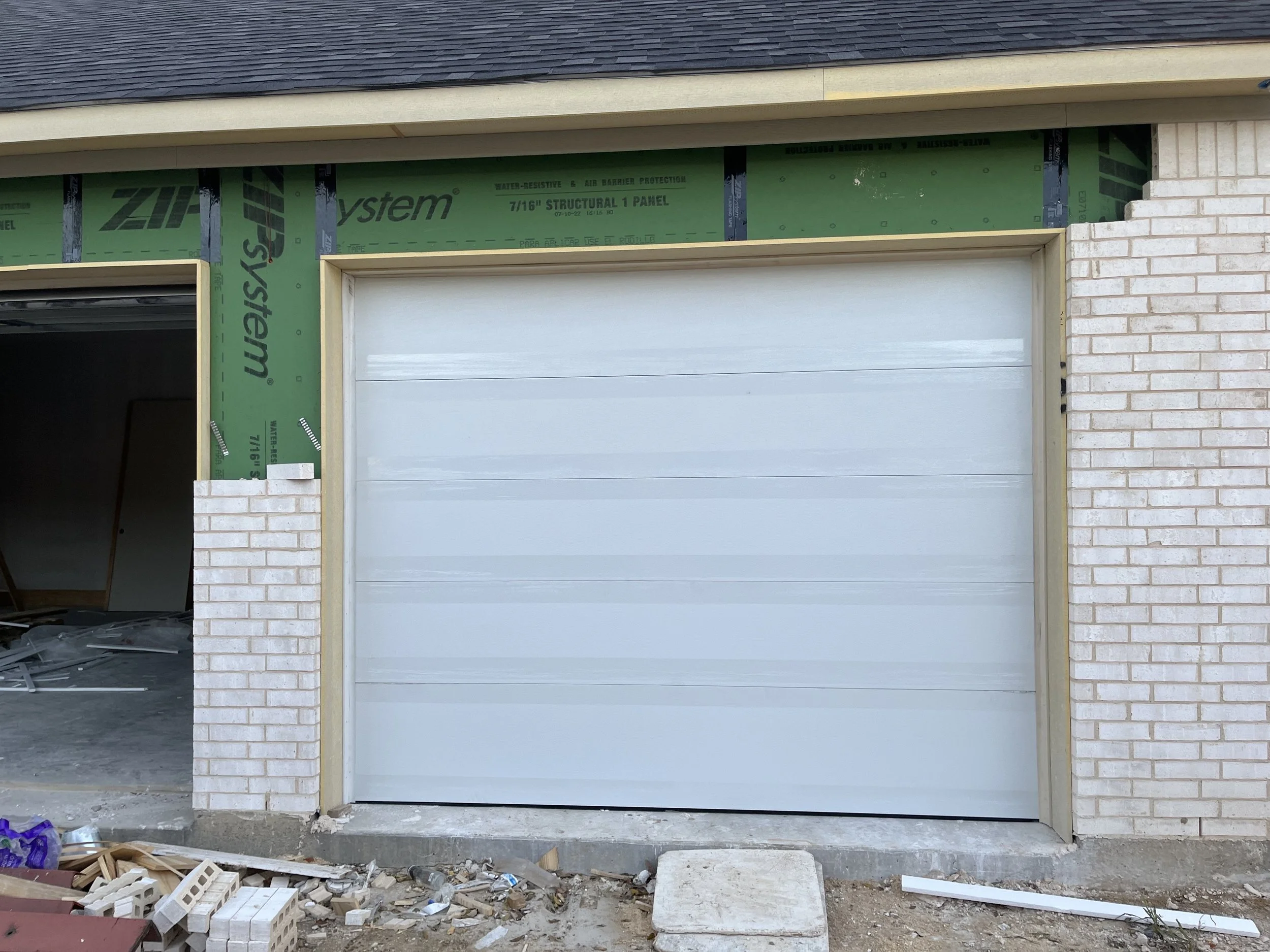 Garage door installation in progress, with books and construction debris on the ground outside a partially built garage.