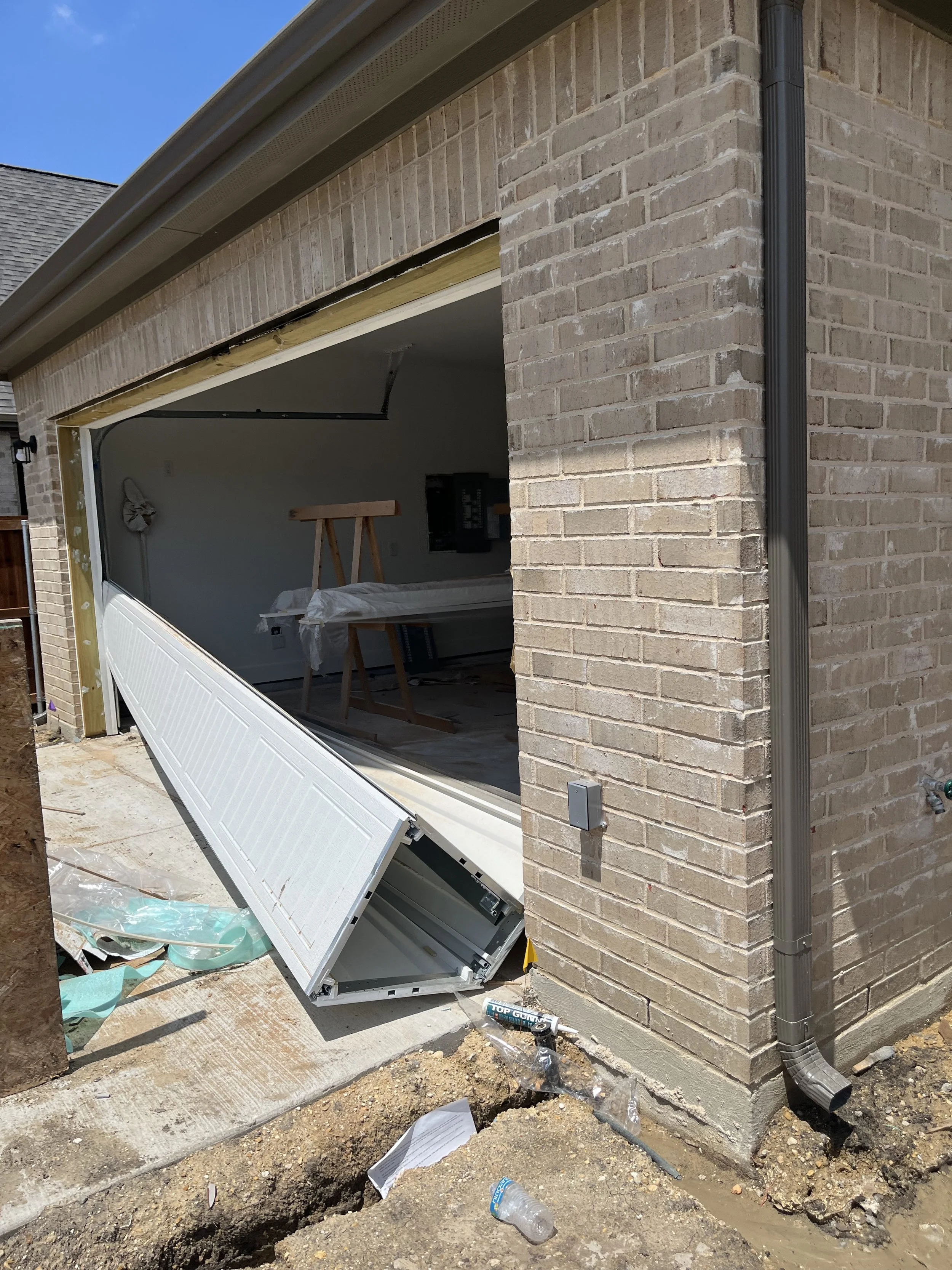 Construction of a garage door in a brick house with construction tools and materials outside.