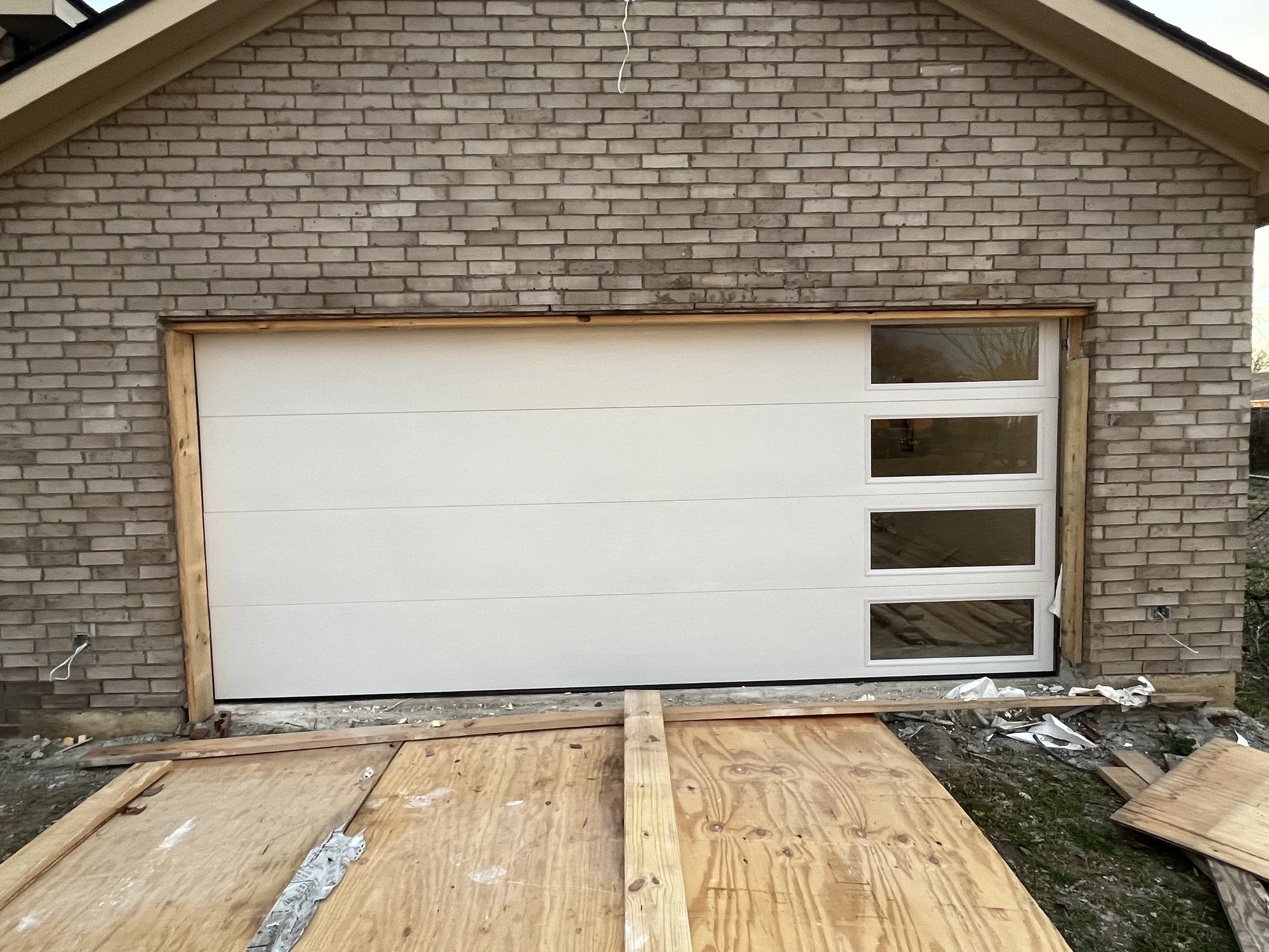 A garage door with four windows on the right side, installed in a brick wall, with construction materials in front.