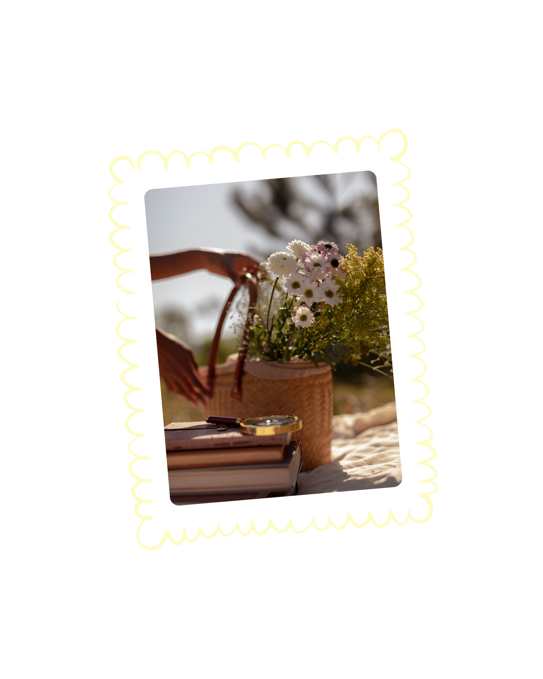 A basket of white daisies and yellow flowers on a table, with a hand reaching in to pick some, blurred background of trees and sky.
