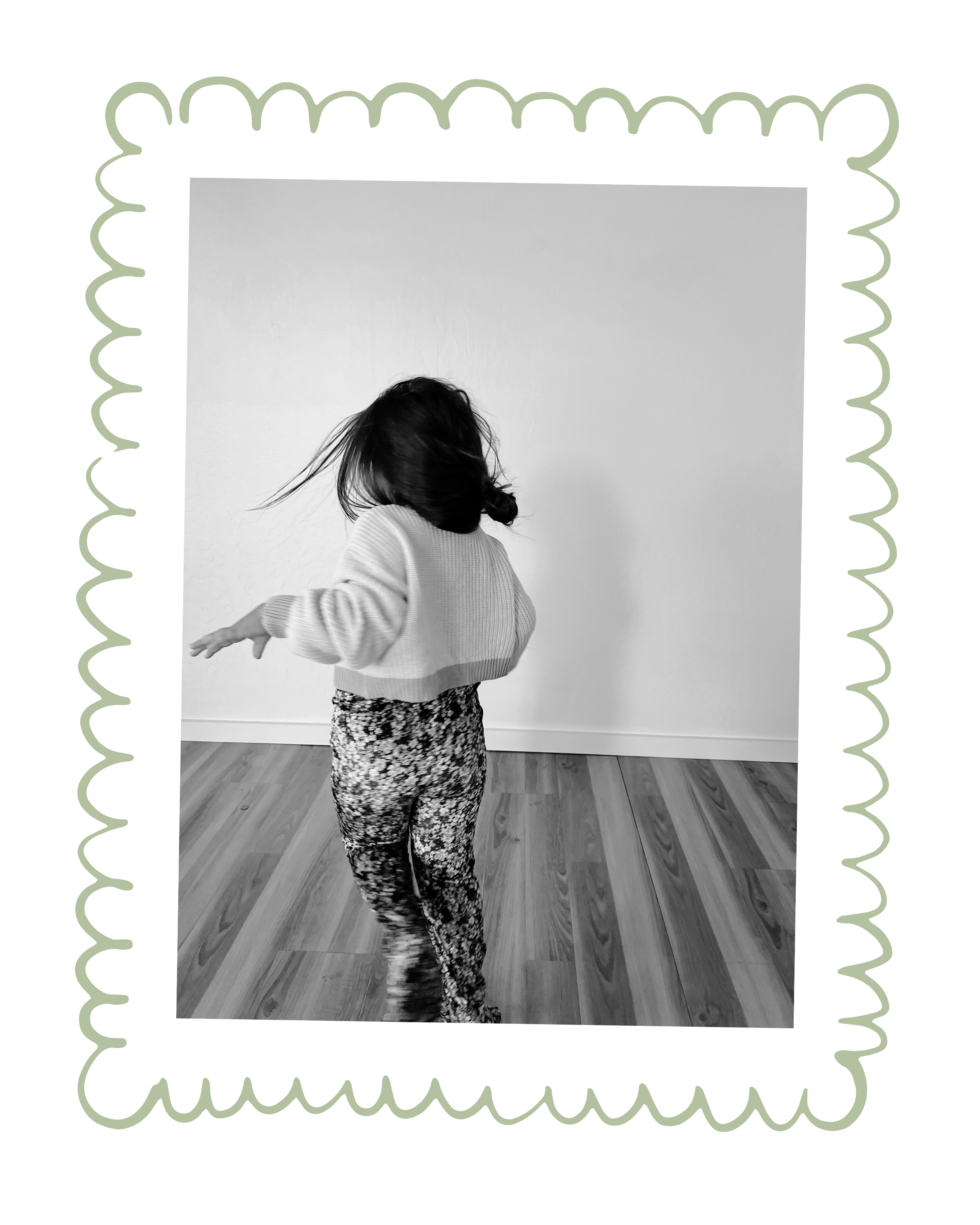 A woman dancing with hair moving, wearing a sweater and patterned pants, standing on a wooden floor against a plain wall.