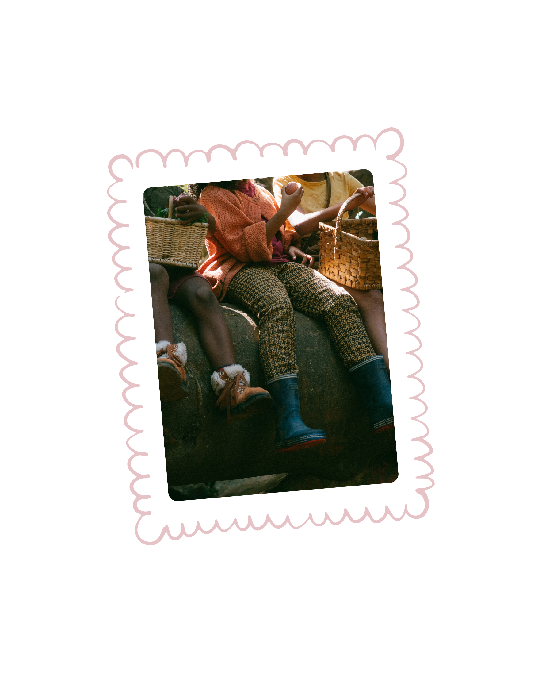 Children sitting on a large rock, holding baskets, wearing boots and cozy clothing.