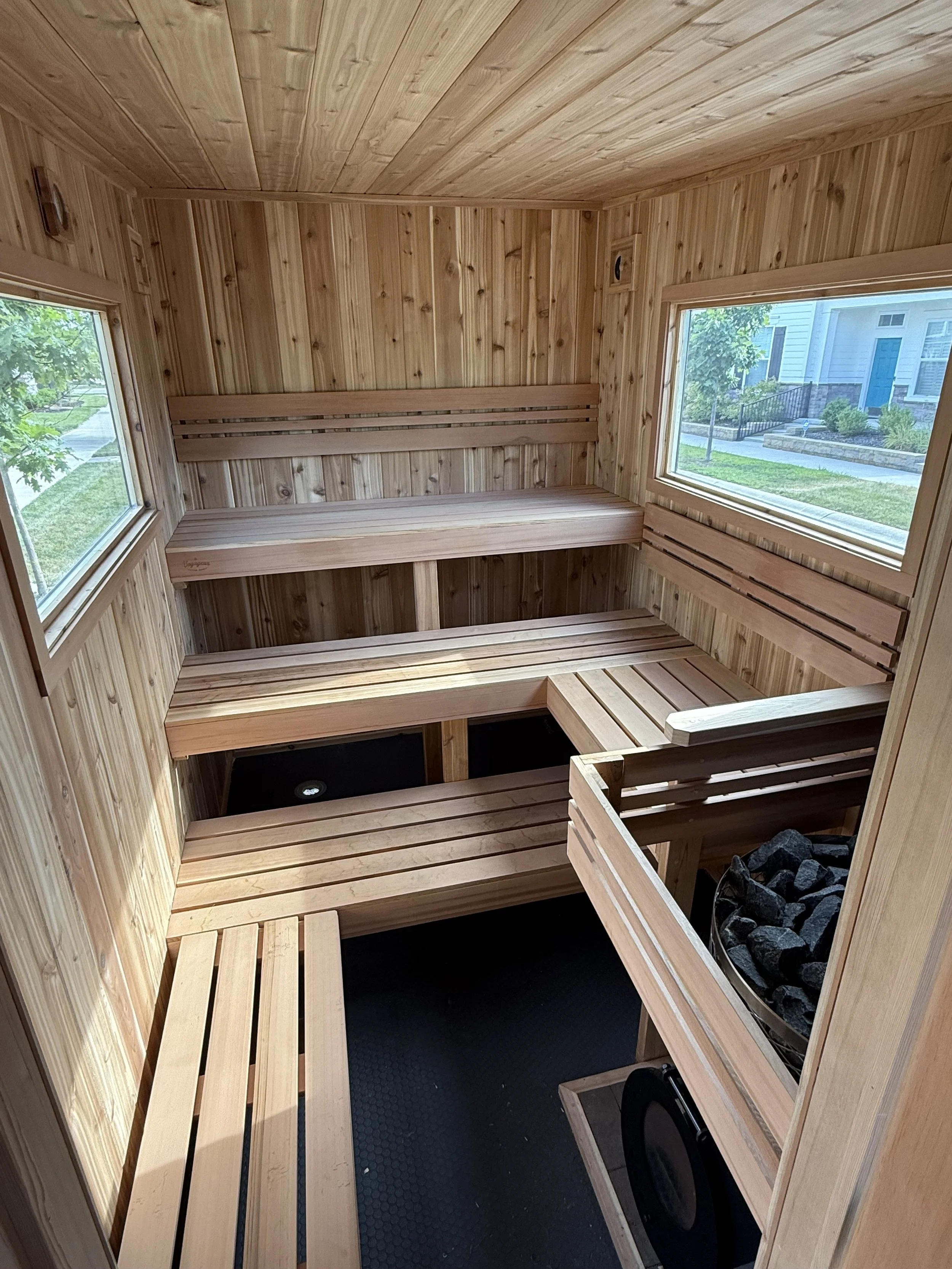 Interior of a traditional Finnish sauna with wooden benches and walls, windows showing an outside view of a residential neighborhood.