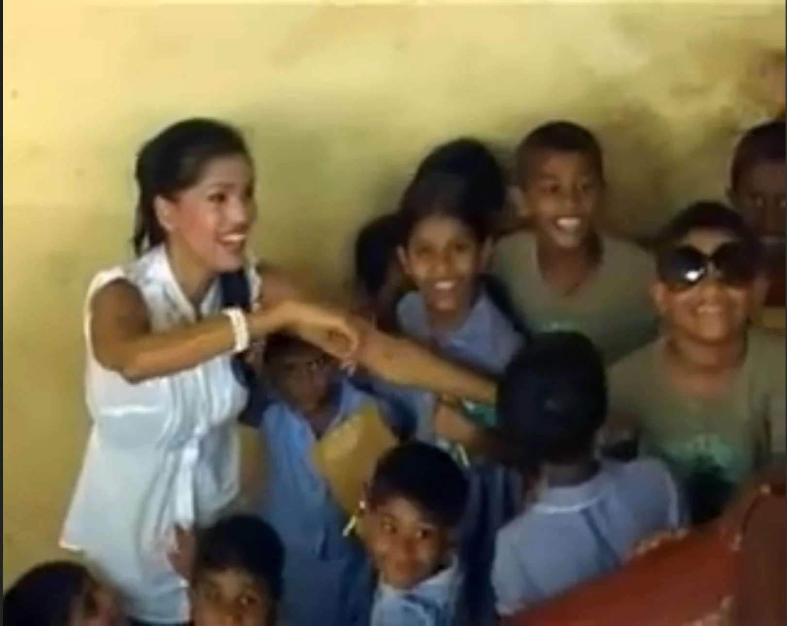 Group of children and a woman smiling and playing together indoors with a yellow wall background.