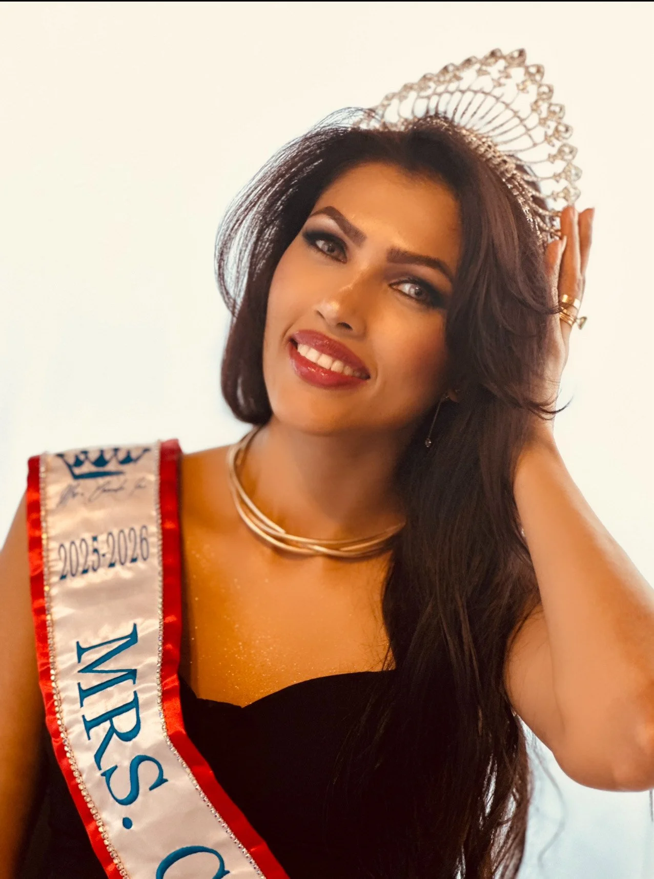 Woman wearing a crown and a sash that reads 'MR'S. 2025-2026,' smiling and posing with her hand on her head.