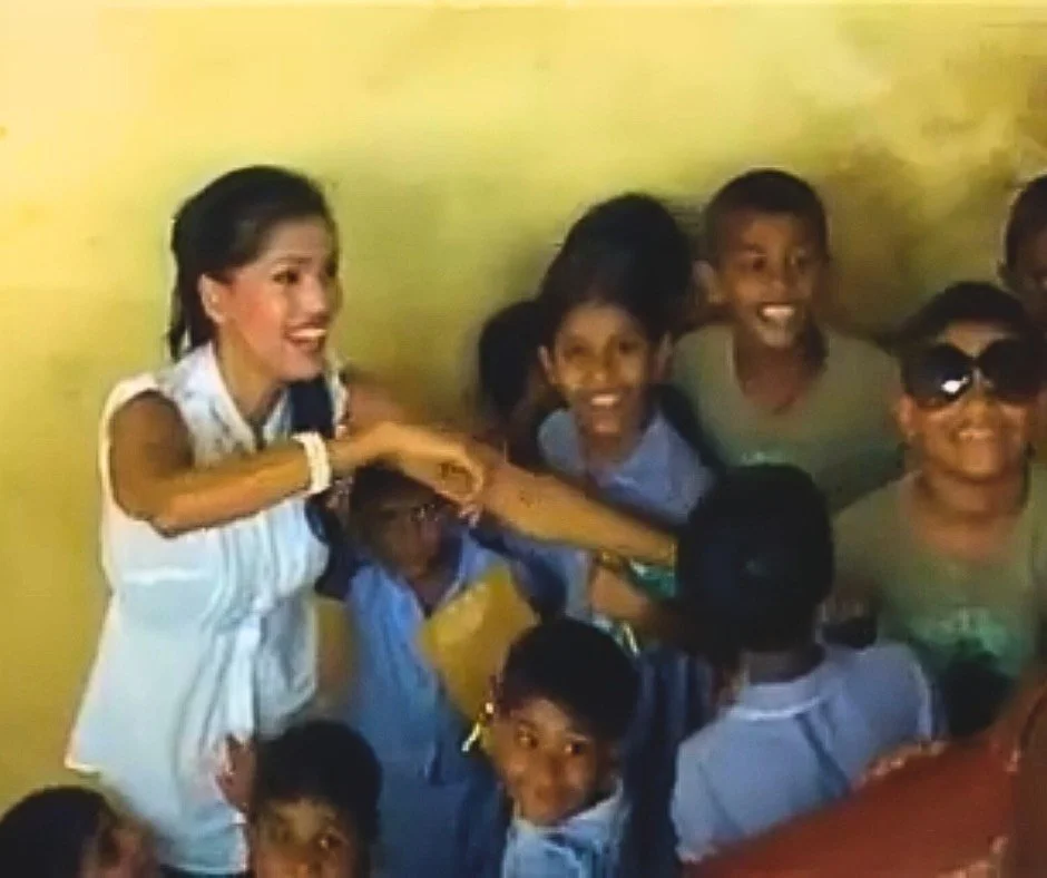 Woman smiling and interacting with a group of children in a room with yellow walls.