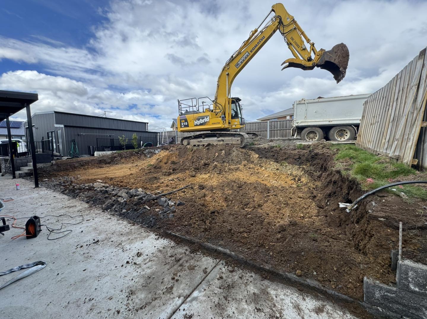 Construction site with a yellow Komatsu excavator lifting a large chunk of dirt, dirt excavation in progress, machinery, and a partly cloudy sky.