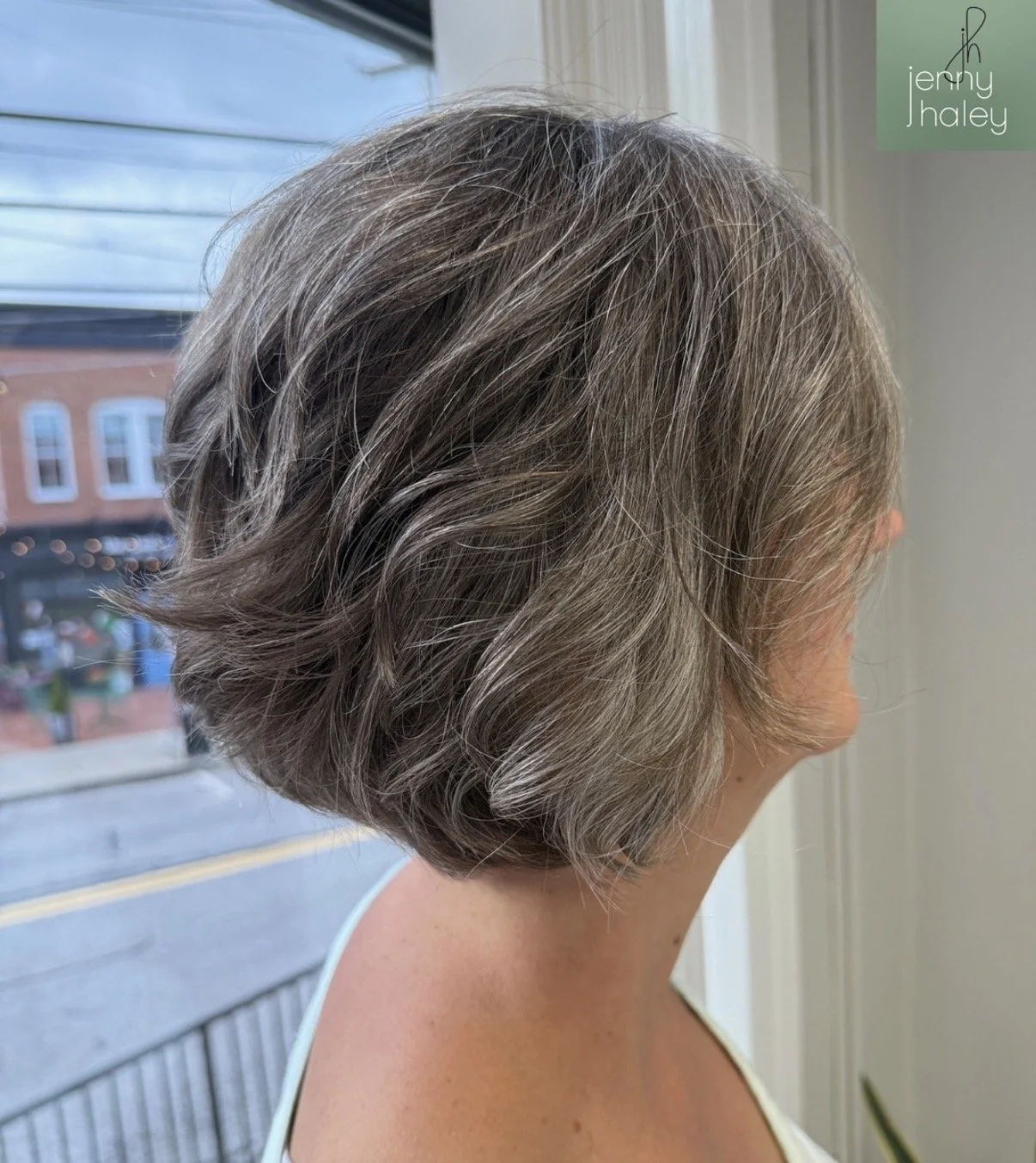 Side view of a woman with short, wavy, gray hair near a window.