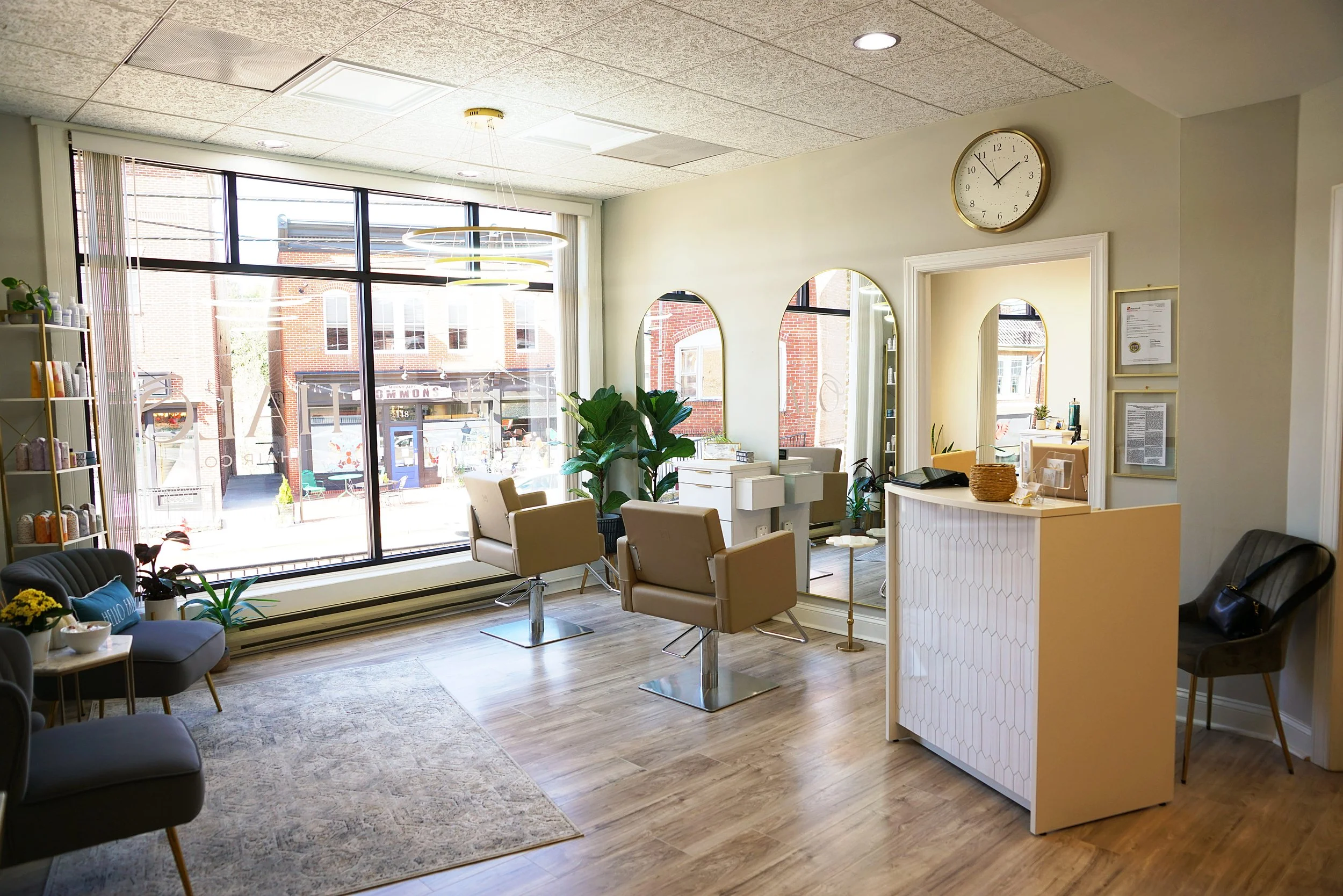 Interior of a modern hair salon or barber shop with large windows, mirrors, chairs, and plants