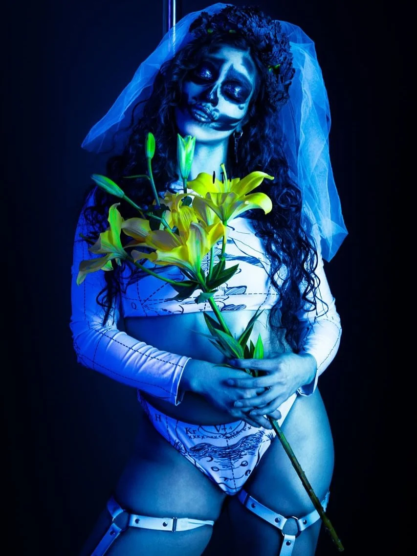 Entre la vida y la muerte, bailo.
Con los lirios como testigos y la piel vestida de arte, abrazo lo ef&iacute;mero, lo oscuro, lo bello.
Soy la novia del abismo, la que danza entre luces azules y flores vivas.
La sensualidad tambi&eacute;n renace en 