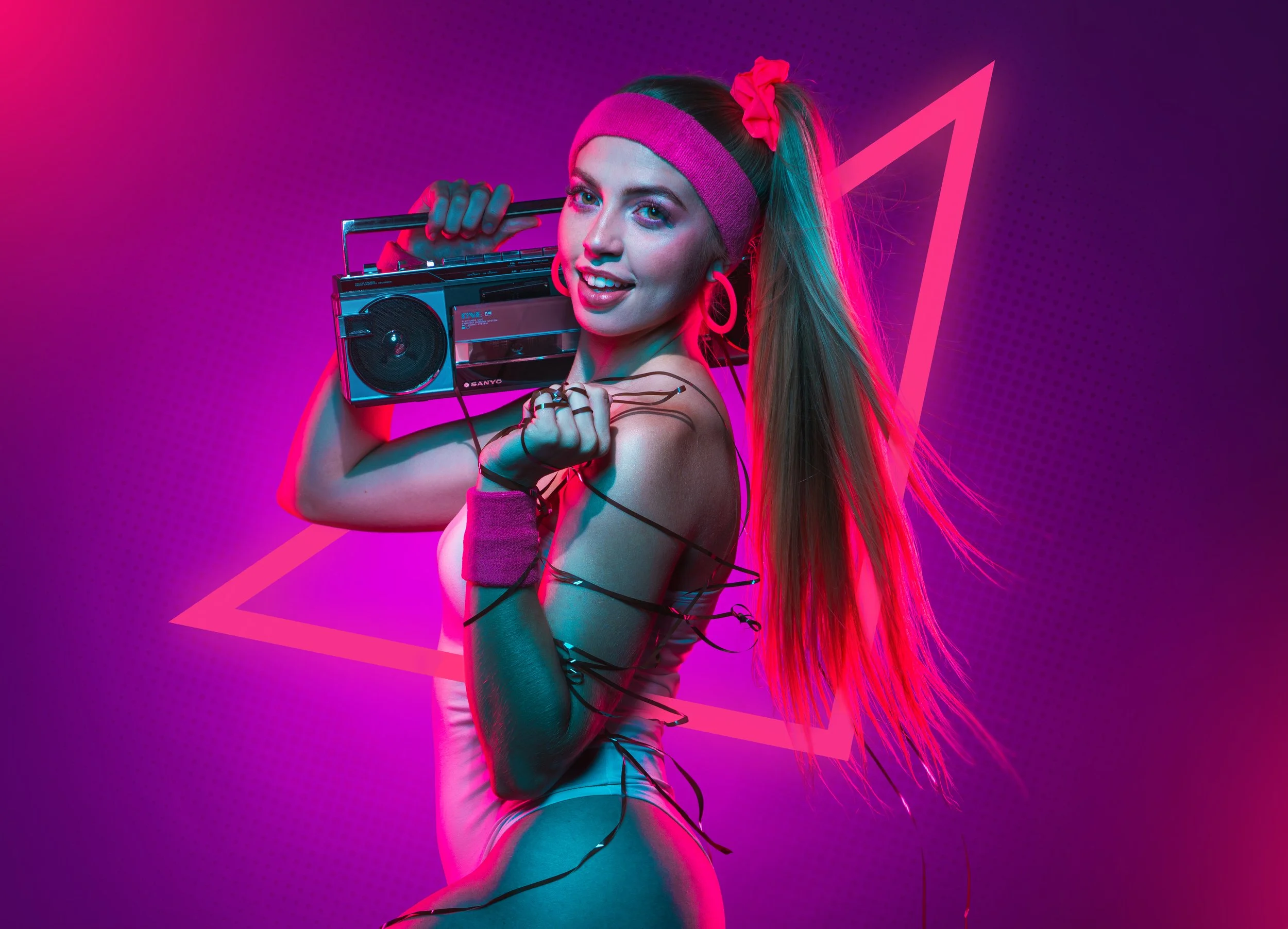 A woman with long hair wearing a pink headband, pink wristbands, and large hoop earrings, holding a vintage boombox on her shoulder, in front of a neon pink triangle backdrop with vibrant blue and pink lighting.