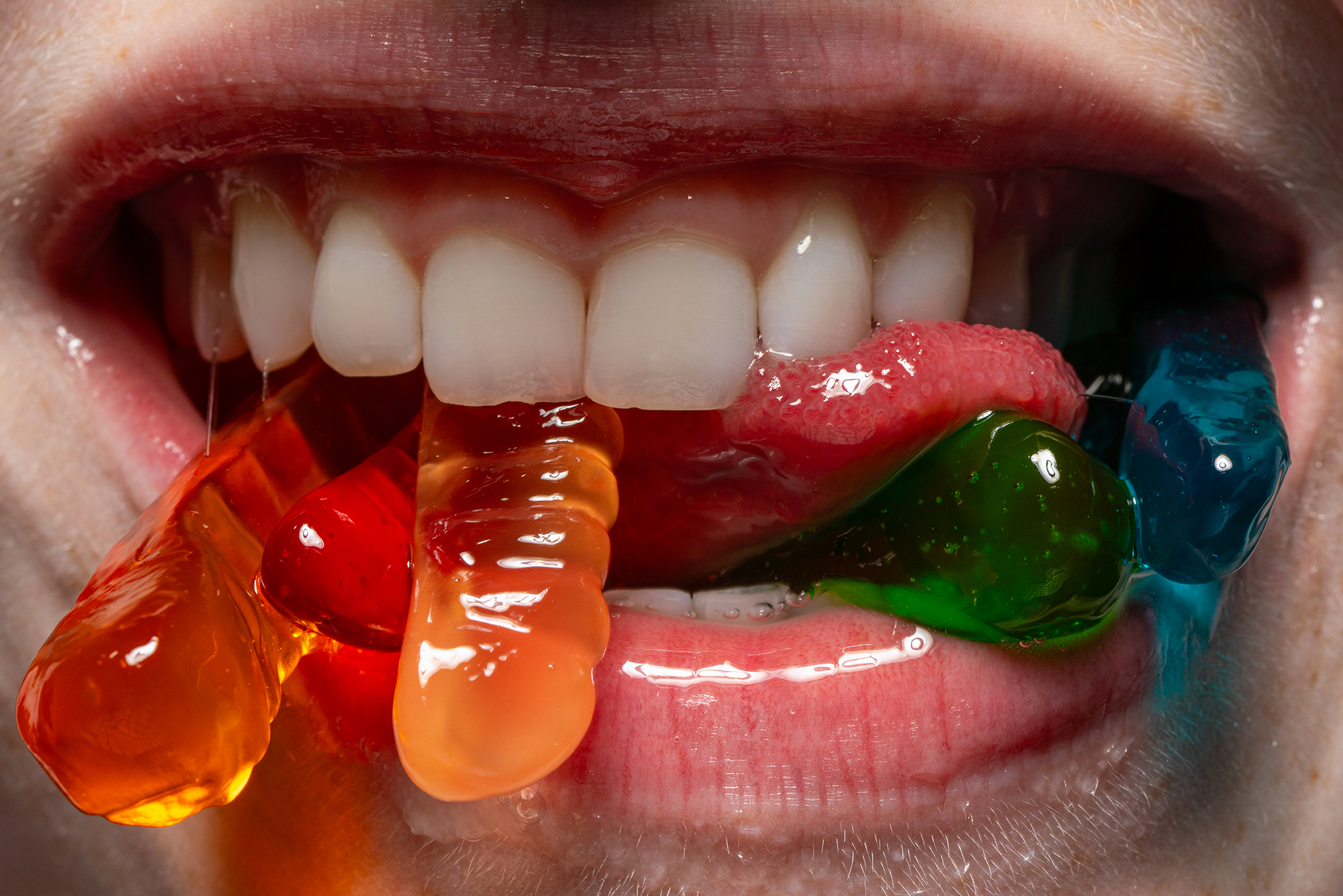 Close-up of a mouth with colorful gummy candies on and around the tongue.