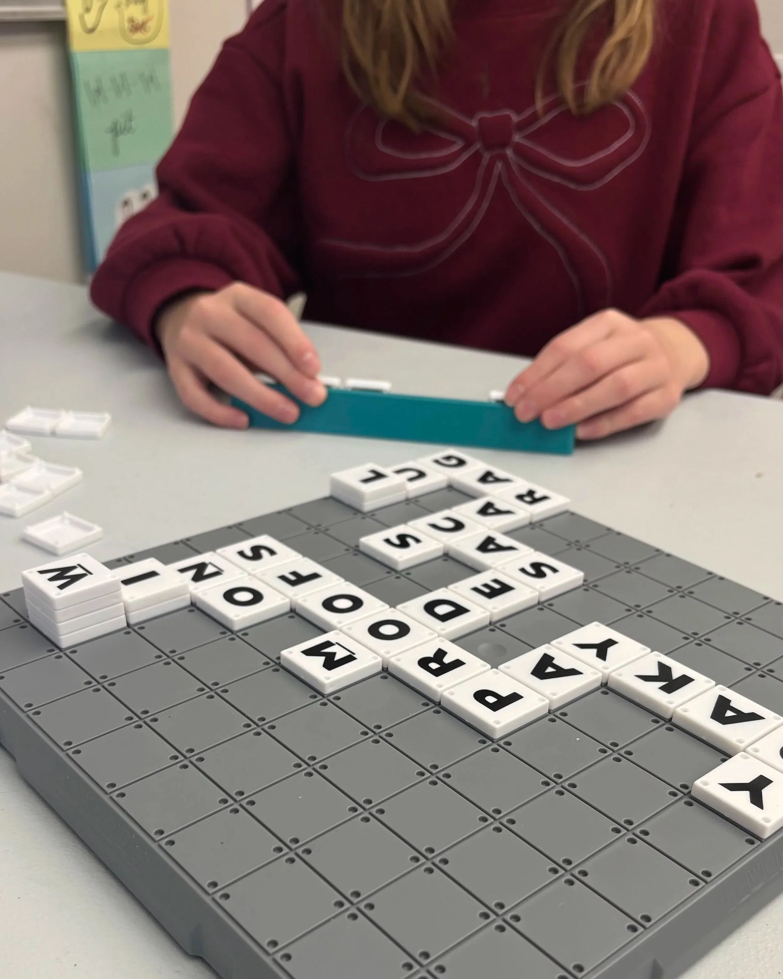 Person playing a game of Scrabble with letter tiles on a gray board, with some tiles spelling words like 'WINK', 'NO', 'SEEDS', and 'A'.