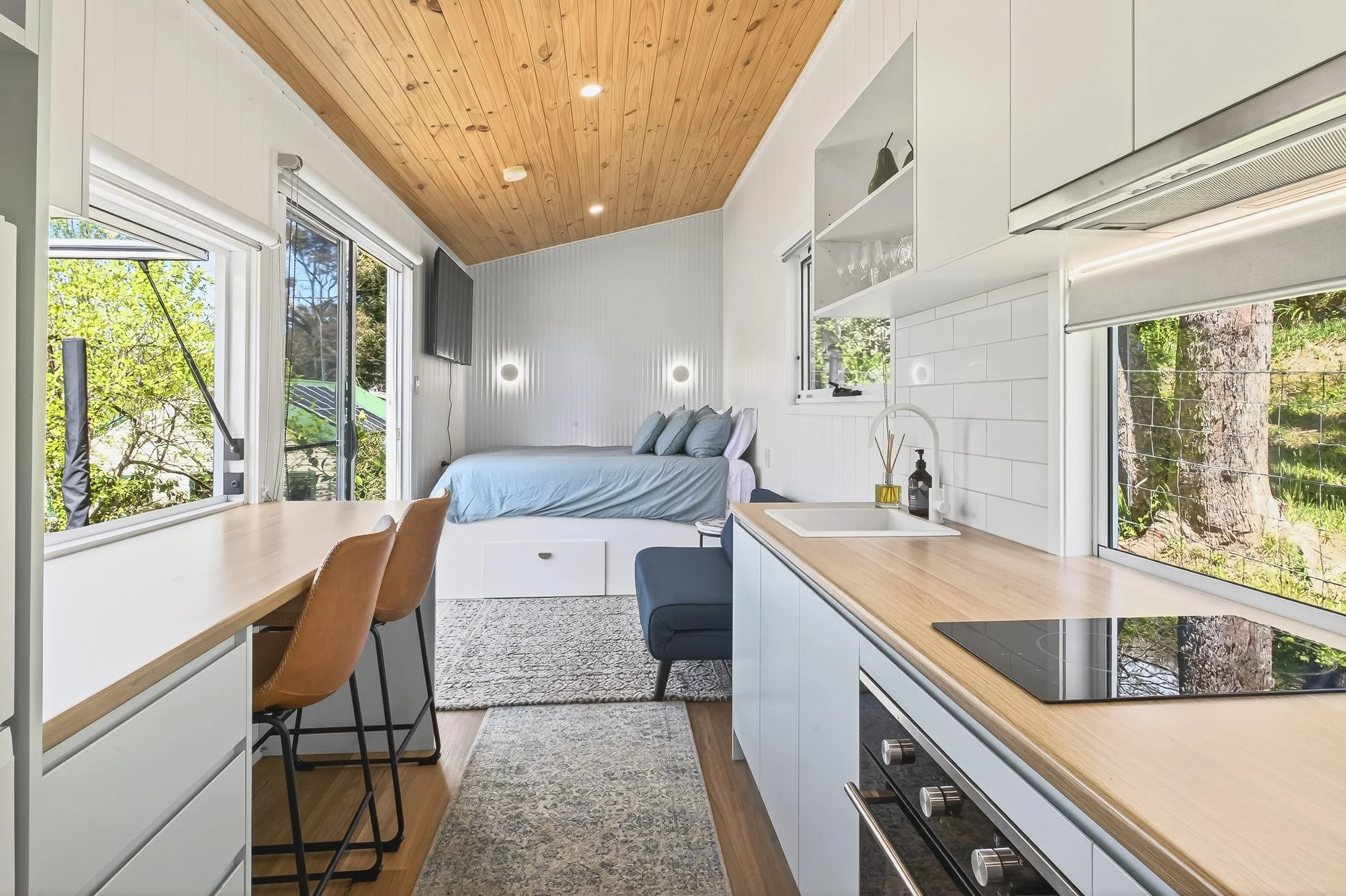 Interior shot of a kitchen area, dining area and bed in a new contemporary tiny home.