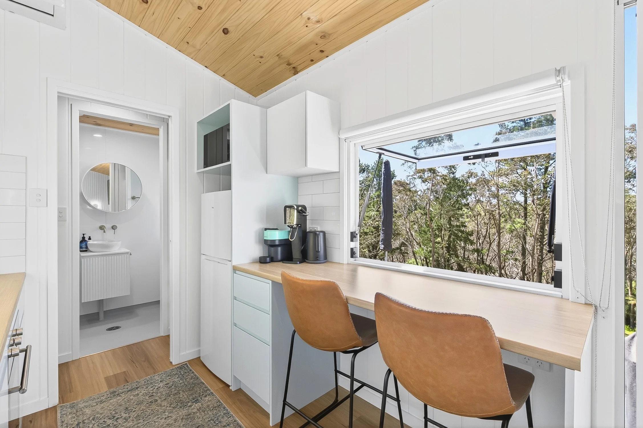 Interior photograph of a tiny home with a bathroom and window opening from the dining area
