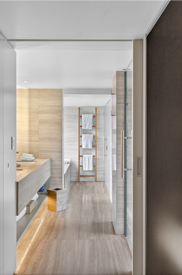 Modern bathroom with wooden ladder towel rack, white towels, light-colored tile flooring, and minimalist design.