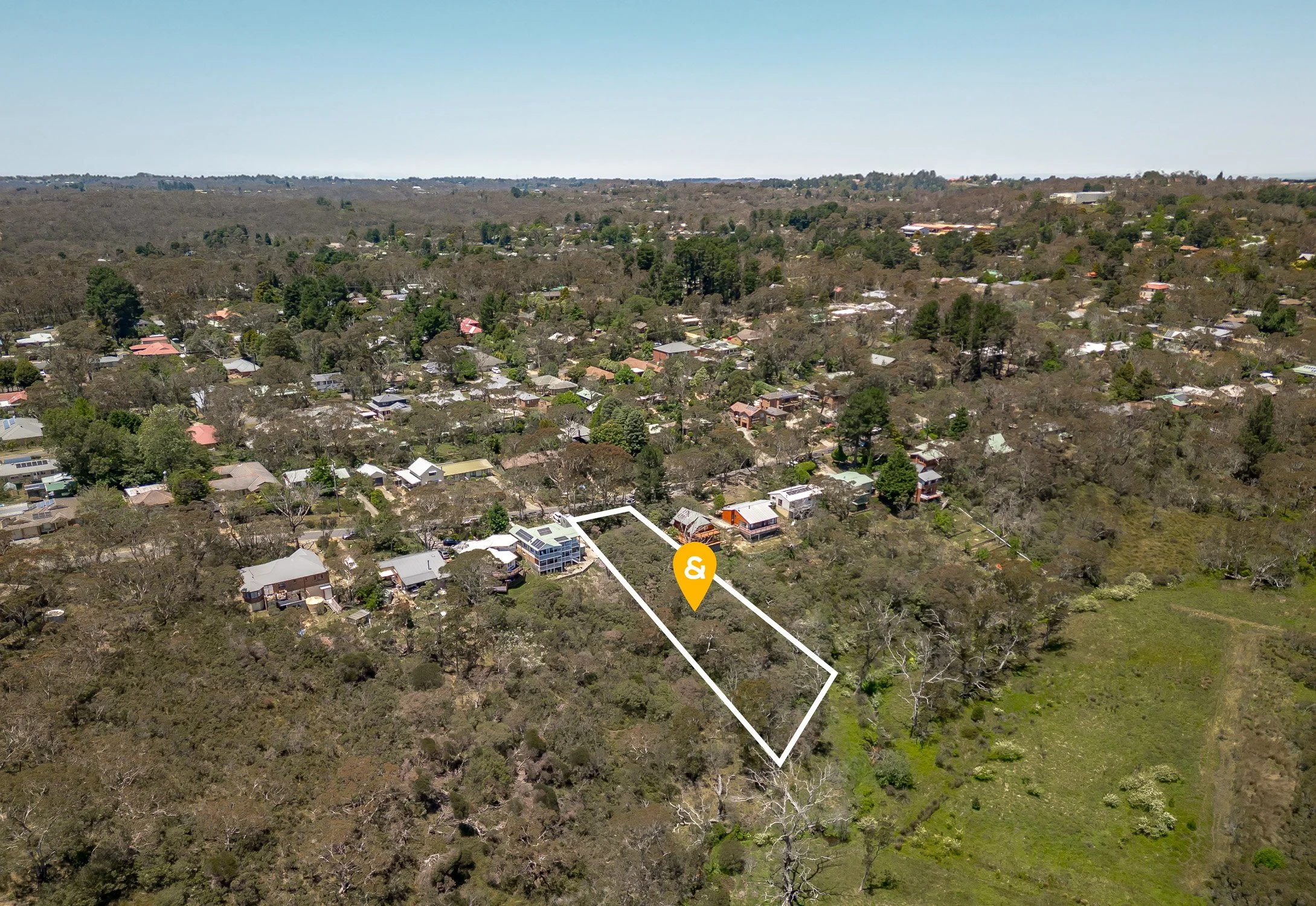 Drone aerial view of a hilly residential neighborhood in Katoomba with numerous houses, trees, and greenery under a clear blue sky.