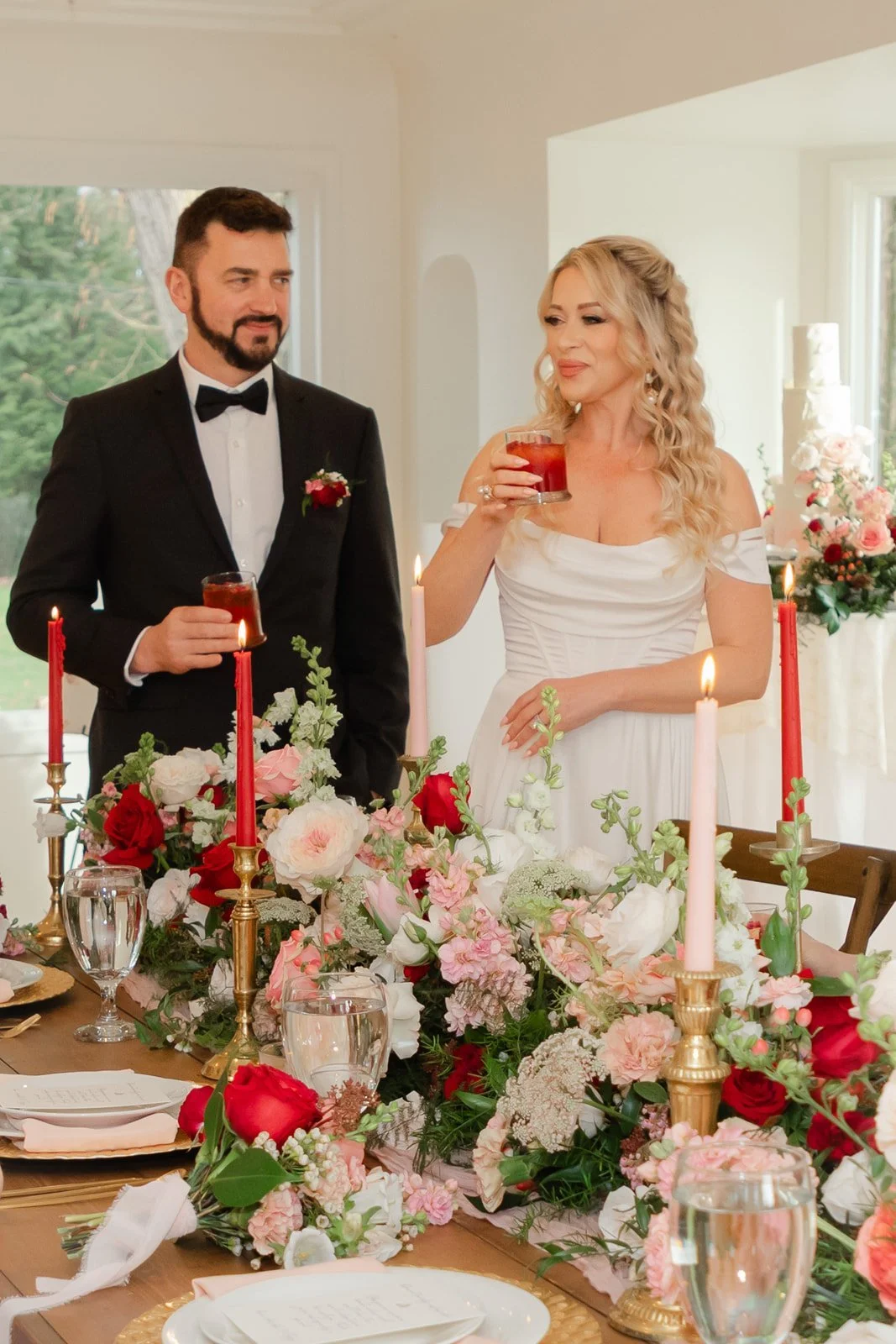 Bride and groom toasting behind a candlelit table of red and pink florals at The Preserve in McMinnville, Oregon