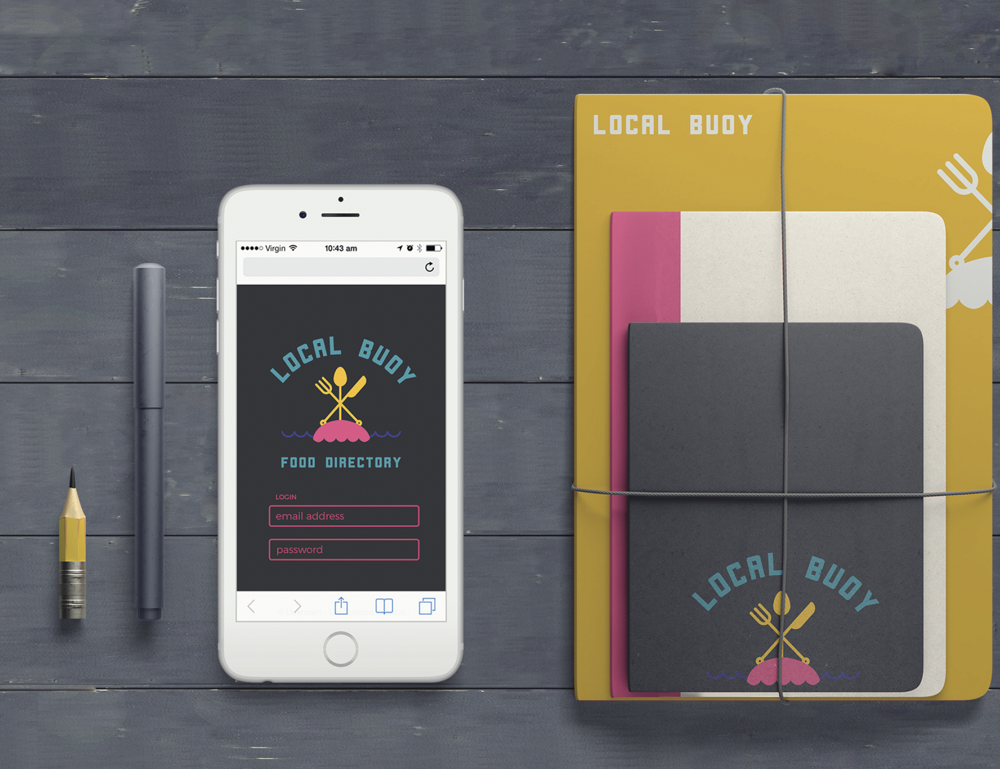 Flat lay of a smartphone displaying a food directory app, a yellow pen, a gray pen, and three notebooks in pink, white, and gray, with the notebooks tied together, on a dark gray wooden surface.