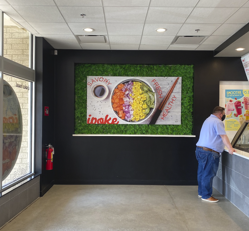 Large digital menu board showing a bowl of poke salad with ingredients like orange salmon, purple onions, yellow corn, and green cucumbers with a cup of sauce, chopsticks, and text describing it as flavorful, fresh, healthy, and savory inside a restaurant.