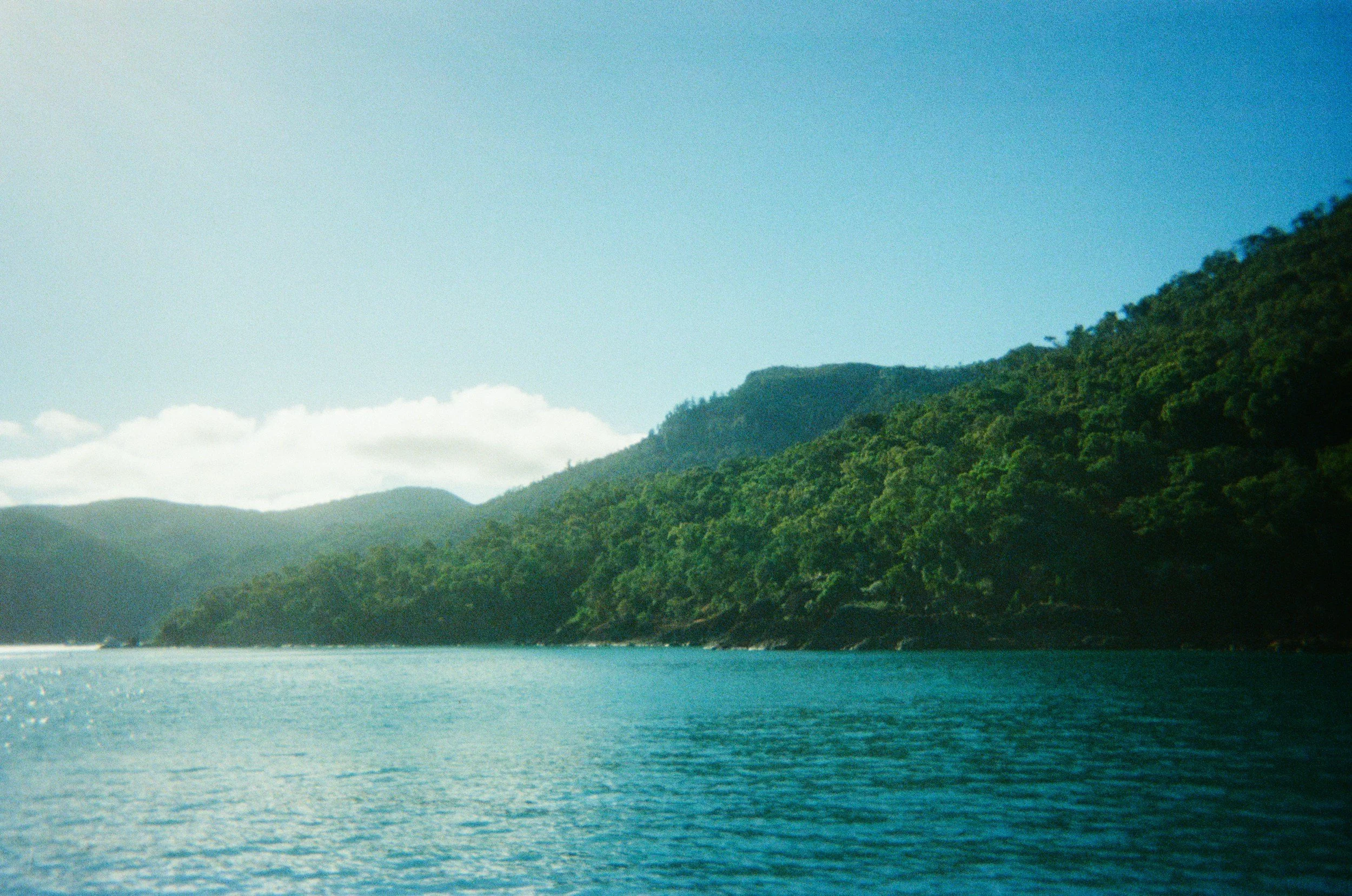 Scenic view of a body of water with green forested hills in the background under a blue sky with some clouds.
