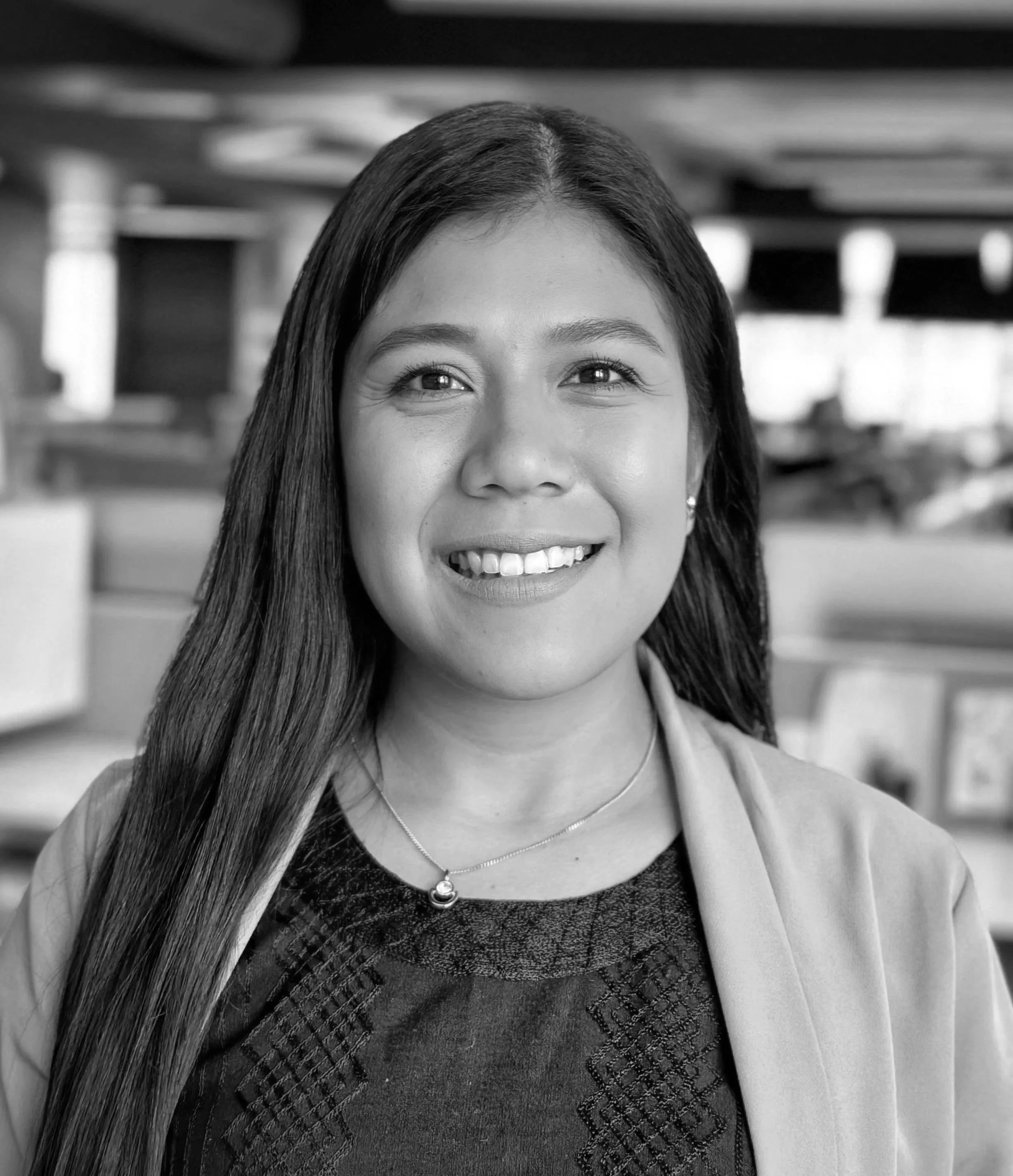 Retrato en blanco y negro de una mujer con una sonrisa brillante, cabello largo, y vestimenta formal, en un entorno interior.