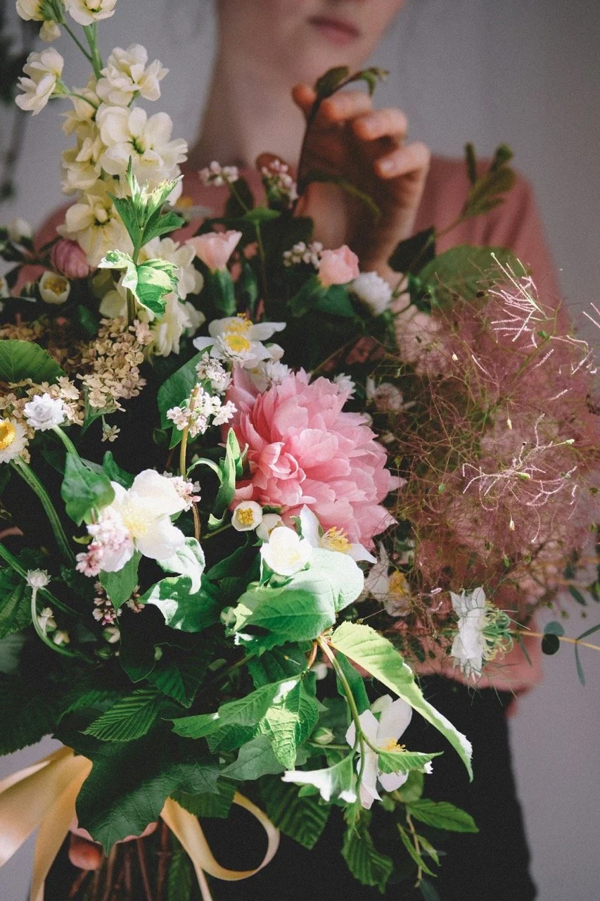 Person holding a bouquet of mixed flowers including peonies, roses, and greenery.