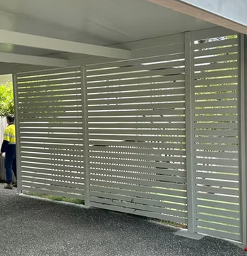 Modern horizontal aluminium slat fence on a building exterior with a small opening near the bottom and a person in a yellow and blue shirt nearby.