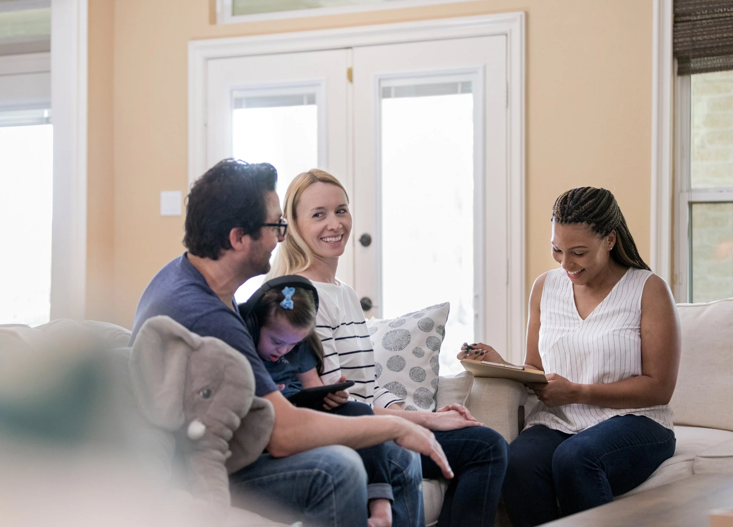 A family of four sitting on a sofa in a living room, with a woman taking notes or filling out paperwork