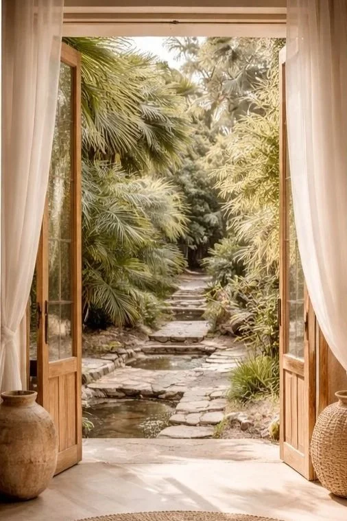 Open patio door looking out onto a lush garden with tropical plants and a stone pathway.