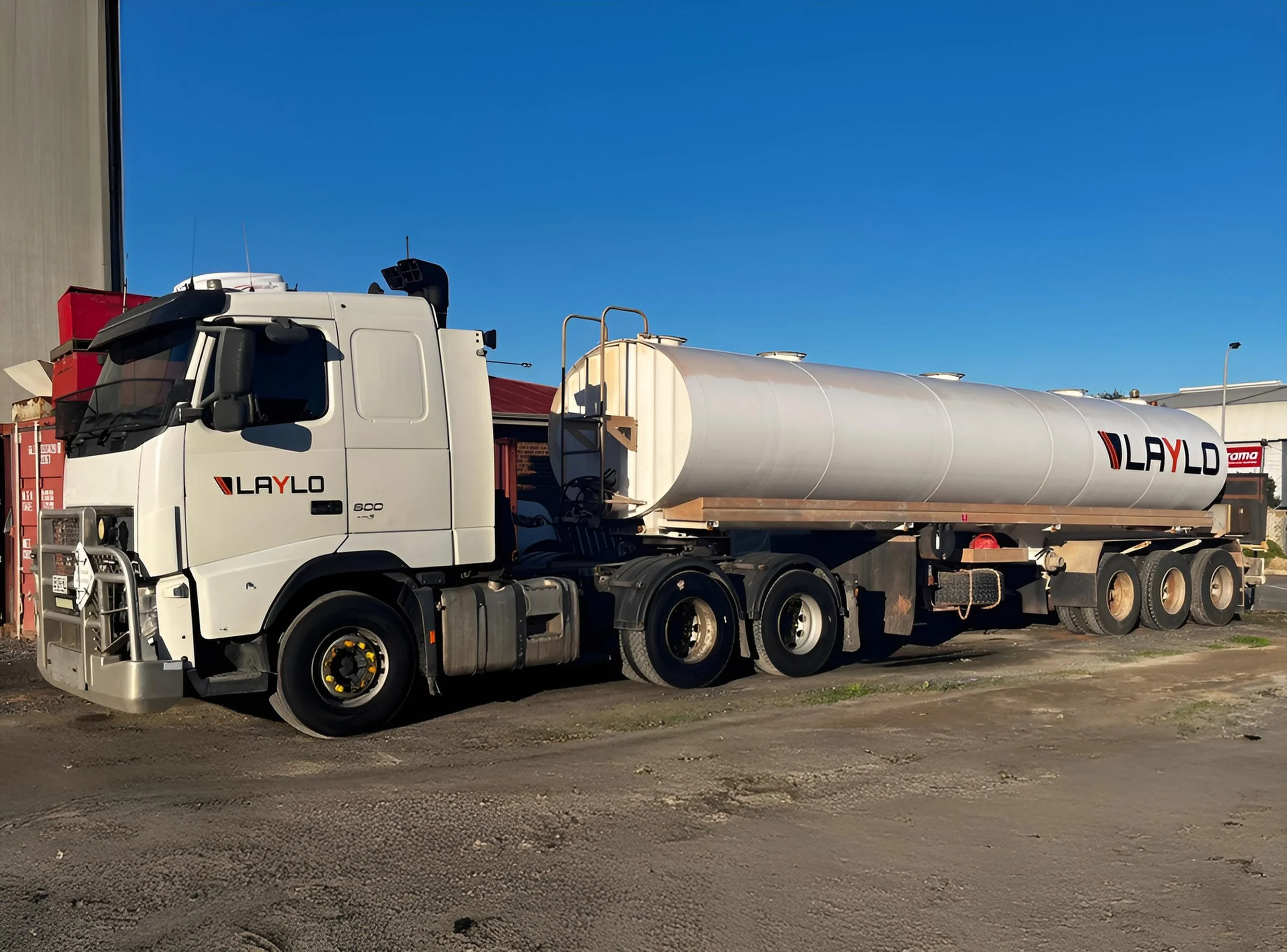 A white tanker truck with the logo 'LAYLO' sitting on a dirt area, with a clear blue sky in the background.