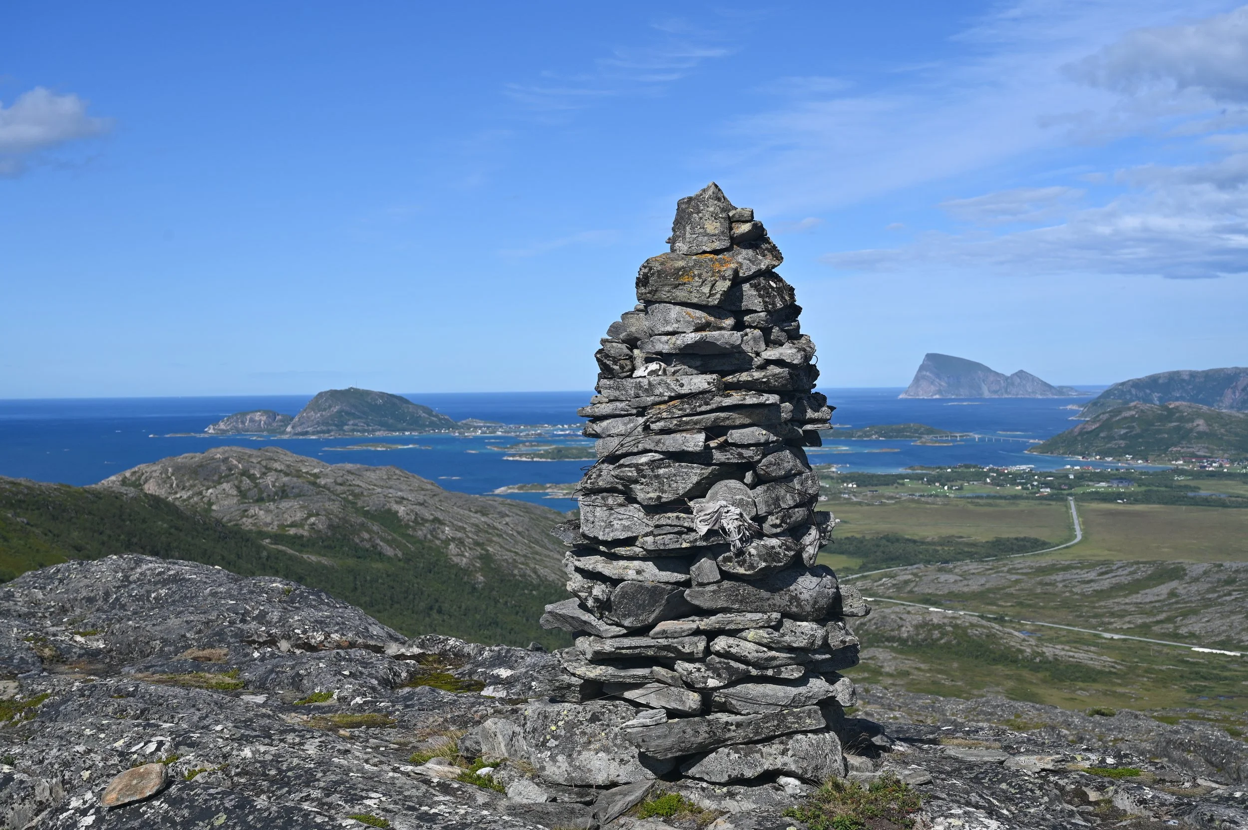 A stone cairn on the summit of Torsnesaksla mountain with panoramic views of Sommarøy, Brensholmen, and the Arctic Ocean – a scenic hiking destination near Tromsø.