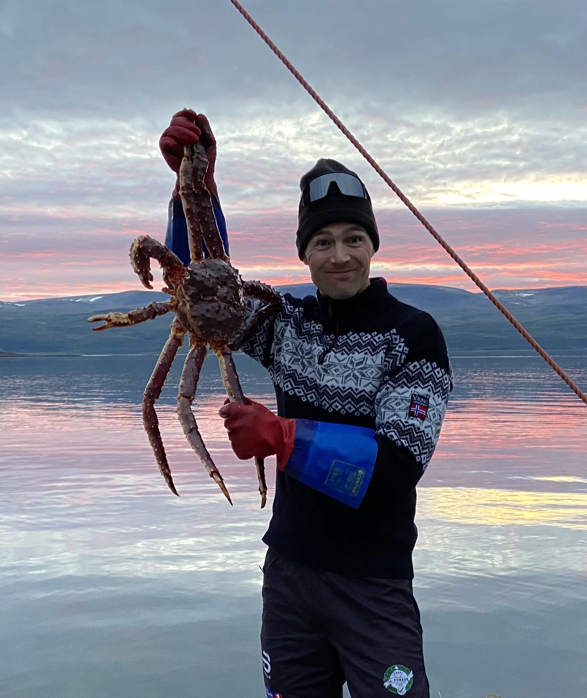 Adventure guide holding a large king crab by the Arctic coast during a polar sunset – a taste of Tromsø’s local culture and nature.