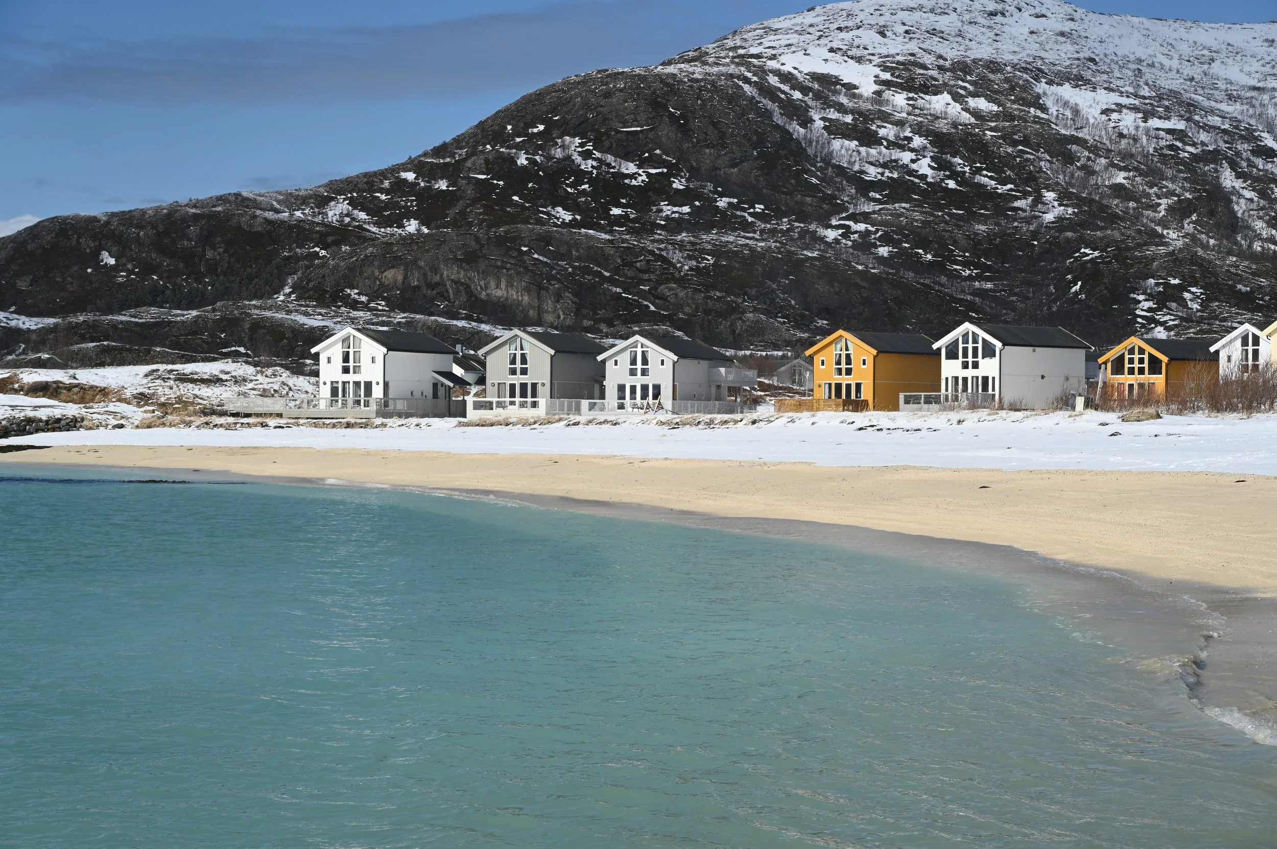 Snow-covered beach and colourful houses in Sommarøy – one of the most scenic coastal villages near Tromsø, Norway.