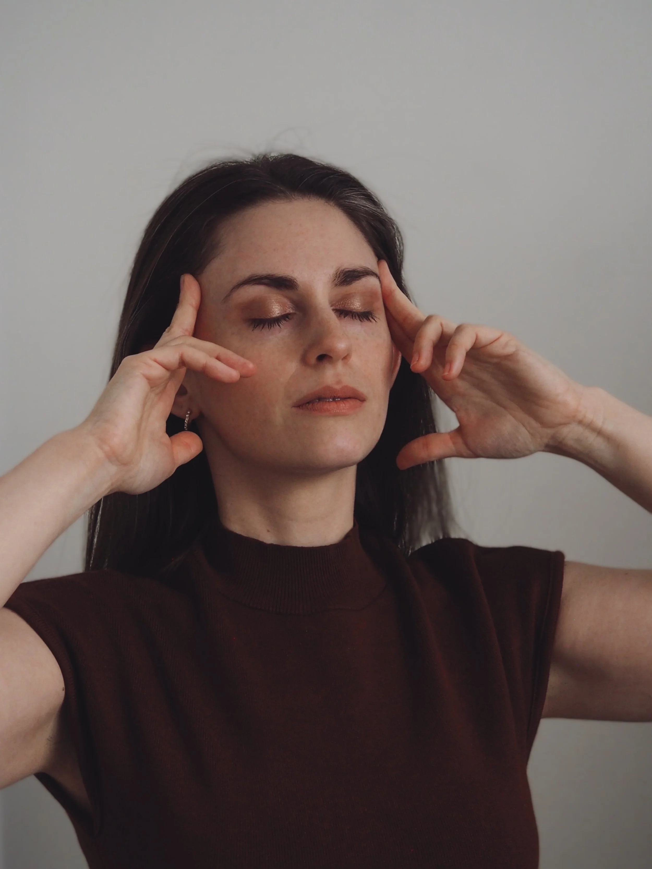 A woman with closed eyes holding her head with both hands.