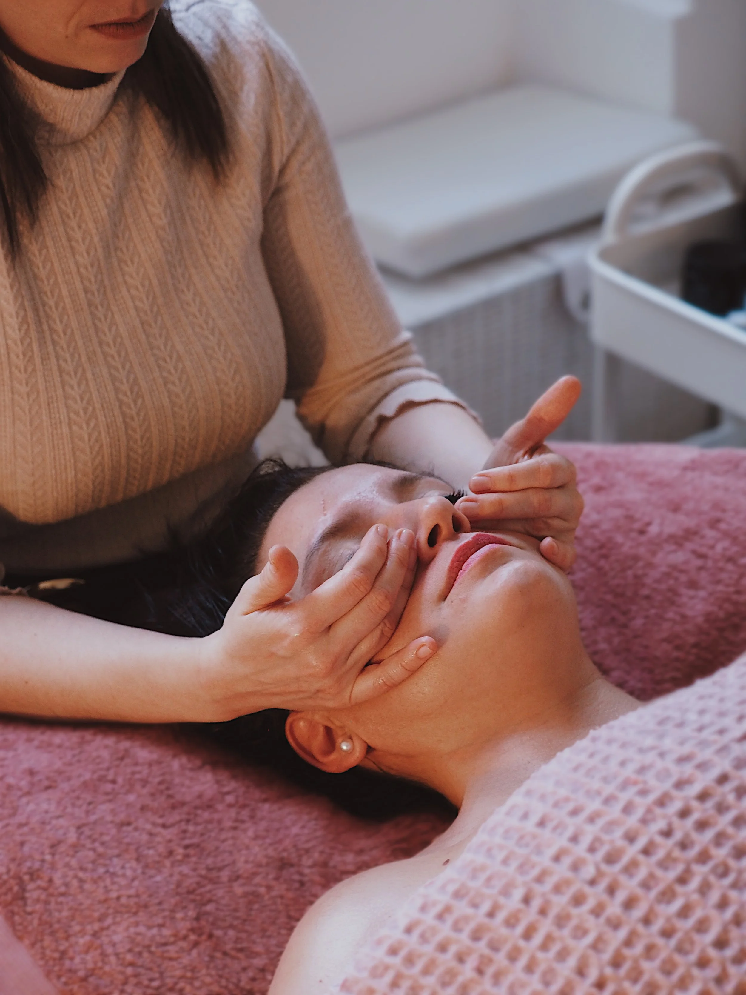 A woman receiving a facial massage from a therapist in a spa setting.