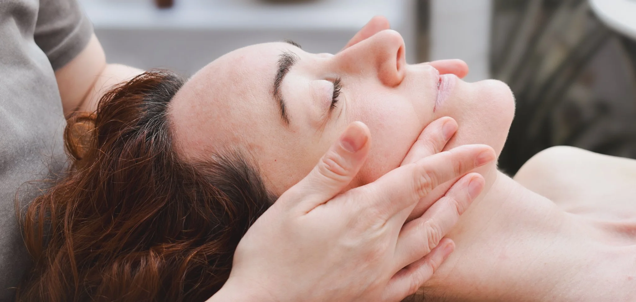 A woman receiving a facial massage in London to reduce jaw pain, TMJ, sculpt her jaw line, natural face lift and improve face lymphatic drainage.