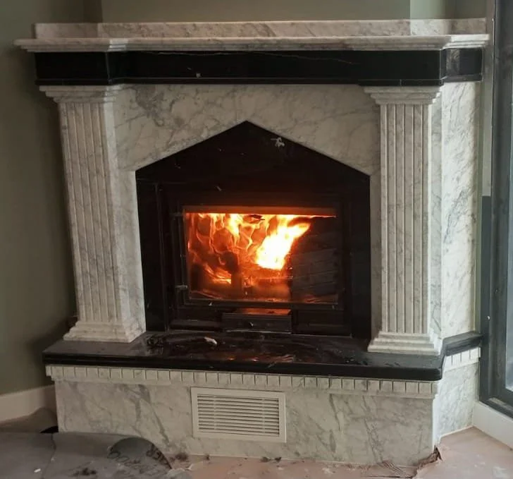 A fireplace with a burning fire inside, framed by a white marble mantel with decorative pillars.