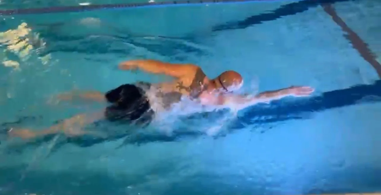 Een persoon zwemt in een zwembad, met een badmuts en bril.