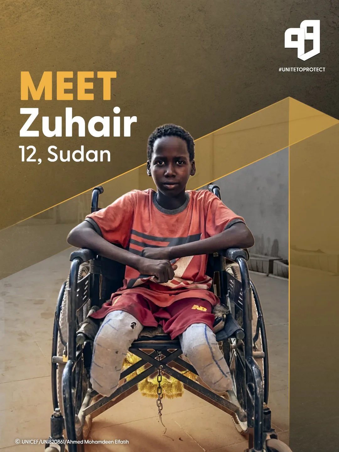 Young boy in a wheelchair with pulled pants, wearing a red and black T-shirt, sitting on a yellow mat indoors