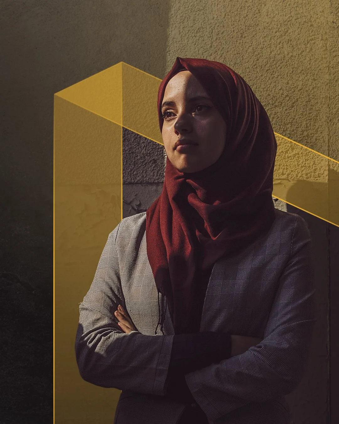 A woman wearing a red headscarf and a checkered blazer stands with her arms crossed outdoors, looking thoughtfully into the distance, with textured wall background and yellow geometric overlay.